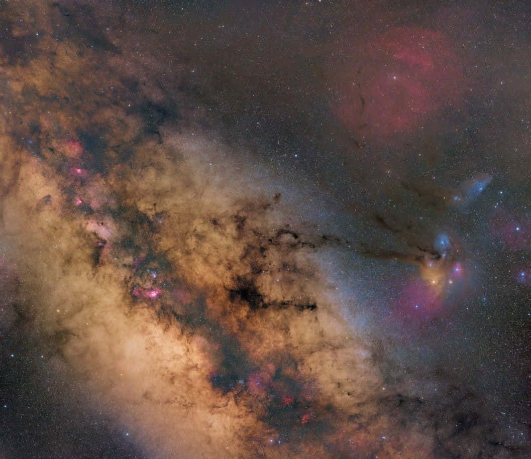 Galactic Center 桌布 壁紙 — 一個宇宙星雲在深空中旋轉，散發著粉紅色和橙色的發光雲團，背景是星場。