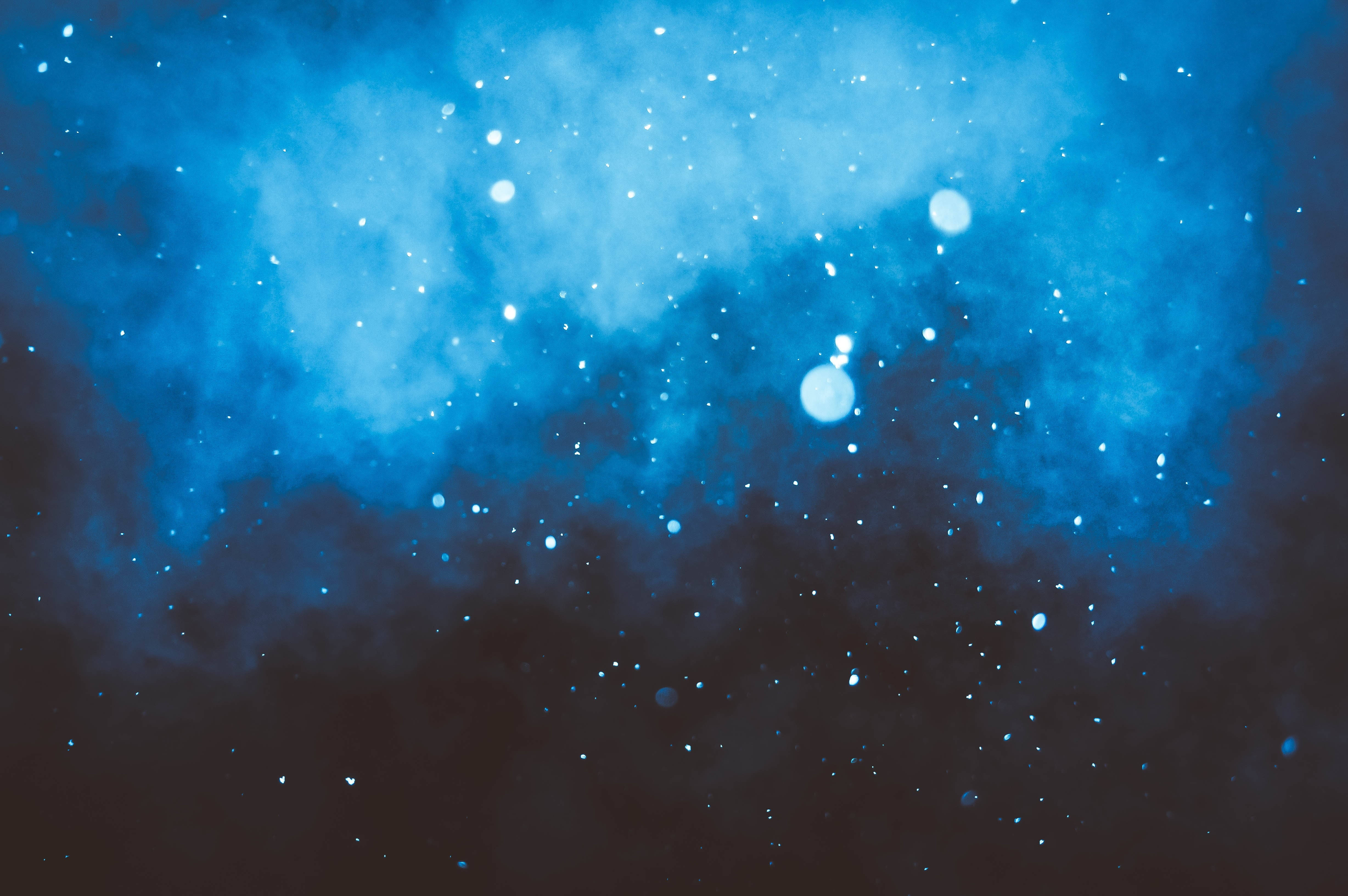 銀河 桌布 壁紙 — 一個宇宙星雲在深藍色和黑色中旋轉，點綴著發光的星星和柔和的光暈。