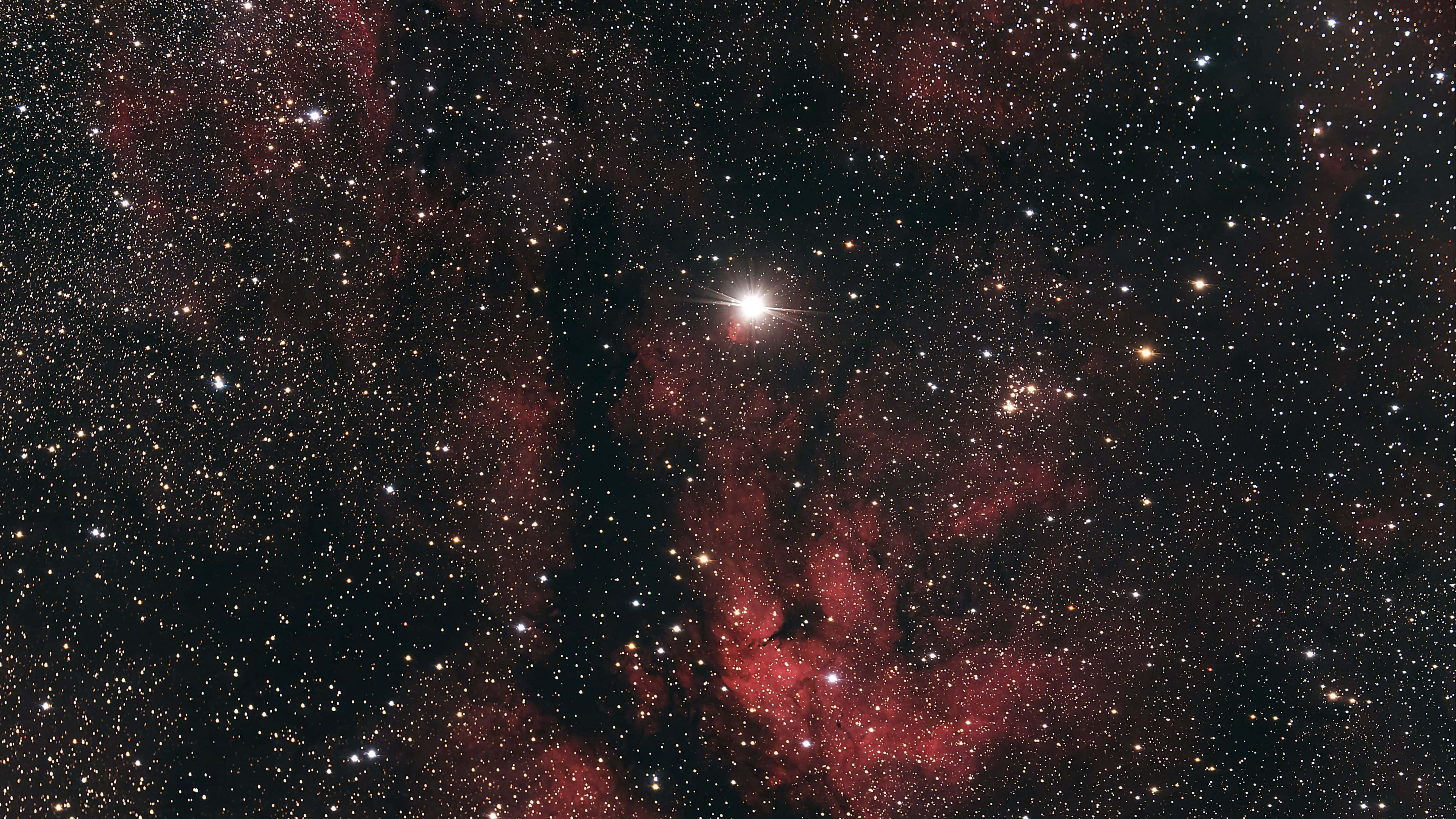 Starry 桌布 壁紙 — 一個宇宙景觀，發光的紅色星雲和無數恆星在深邃的黑色虛空中，中央有一顆明亮的恆星。