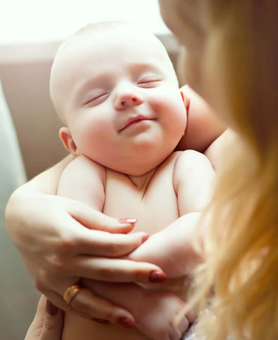 Infant 桌布 壁紙 — 一個安詳熟睡的嬰兒被溫柔地抱在女人的懷裡，柔和自然光突顯他們平靜的表情。