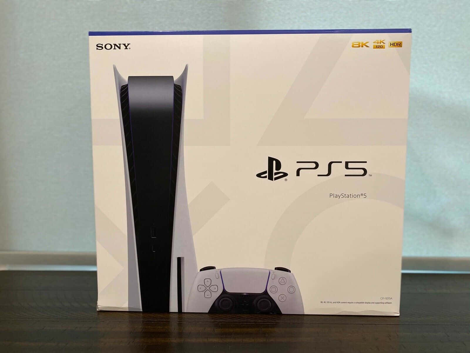 PS5 動態圖片 桌布 壁紙 — 一個完好無缺的PlayStation 5主機盒直立於深色木質表面上，背景是柔和的藍色牆壁。