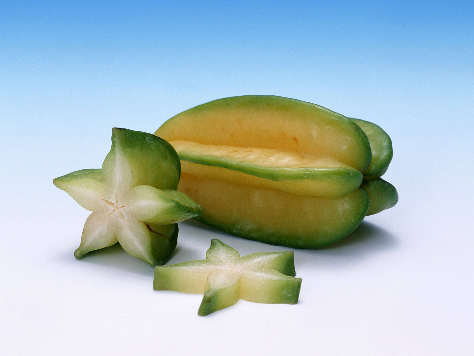 Fruit 桌布 壁紙 — 一個完整和切片的楊桃排列在漸變藍色背景上，展示其星形橫截面。