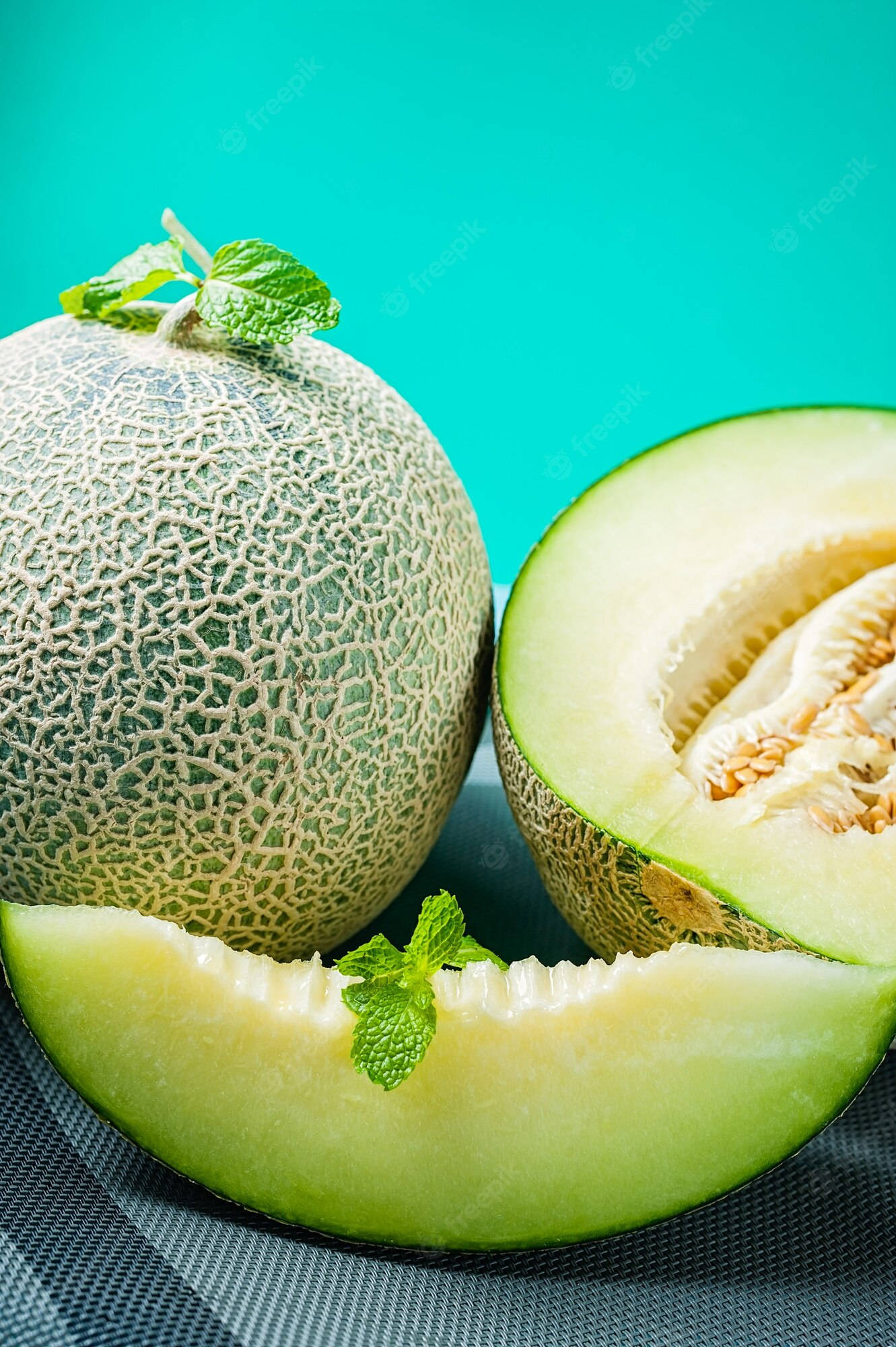 Fruits 桌布 壁紙 — 一個完整和切開的哈密瓜，配上新鮮薄荷葉，放在有紋理的灰色表面上，背景是鮮豔的青色。