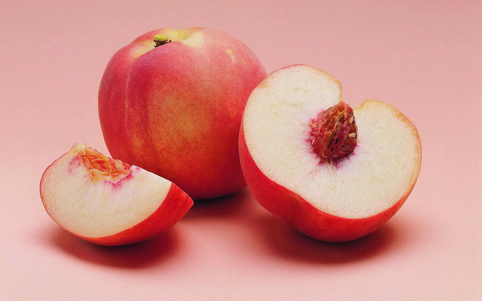 Peach 桌布 壁紙 — 一個完整和切開的成熟桃子，多汁的白色果肉和絨毛的紅色果皮，放在柔軟的粉紅色背景上。