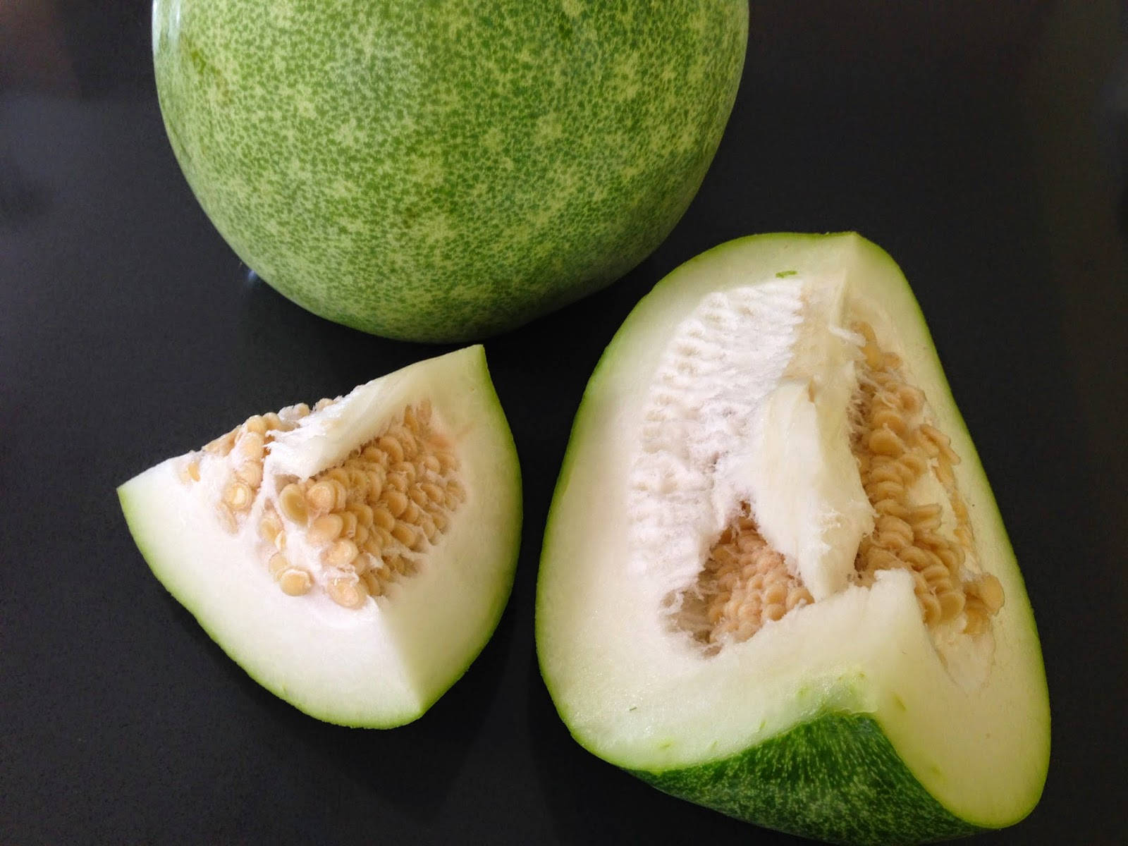 sliced 桌布 壁紙 — 一個完整和切開的青瓜，帶有淡色果肉和種子，放在深色表面上。