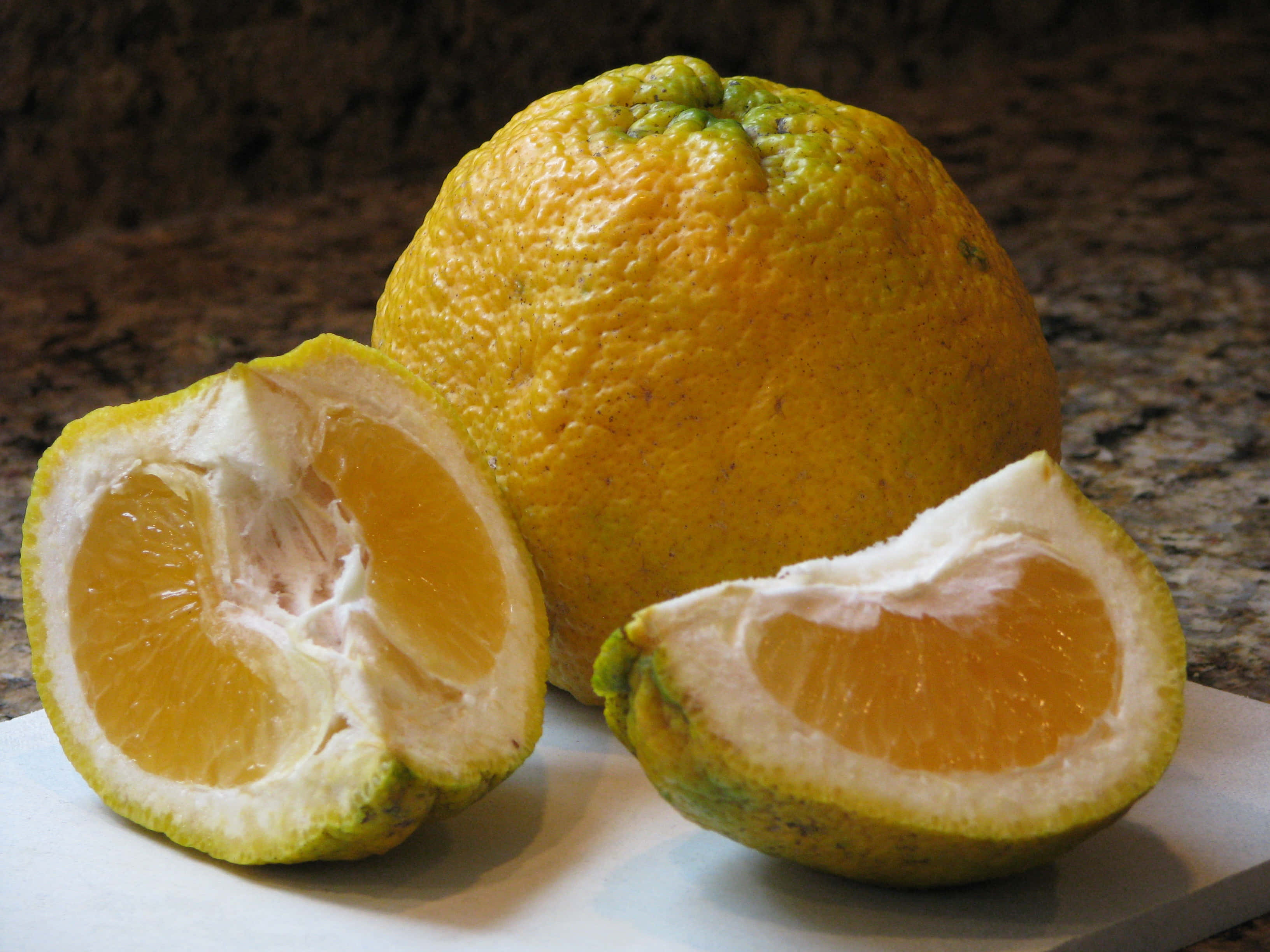 Fruits 桌布 壁紙 — 一個完整和半切的柑橘類水果，帶有充滿活力的橙色果肉和紋理果皮，放在白色砧板上，背景是深色花崗岩檯面。