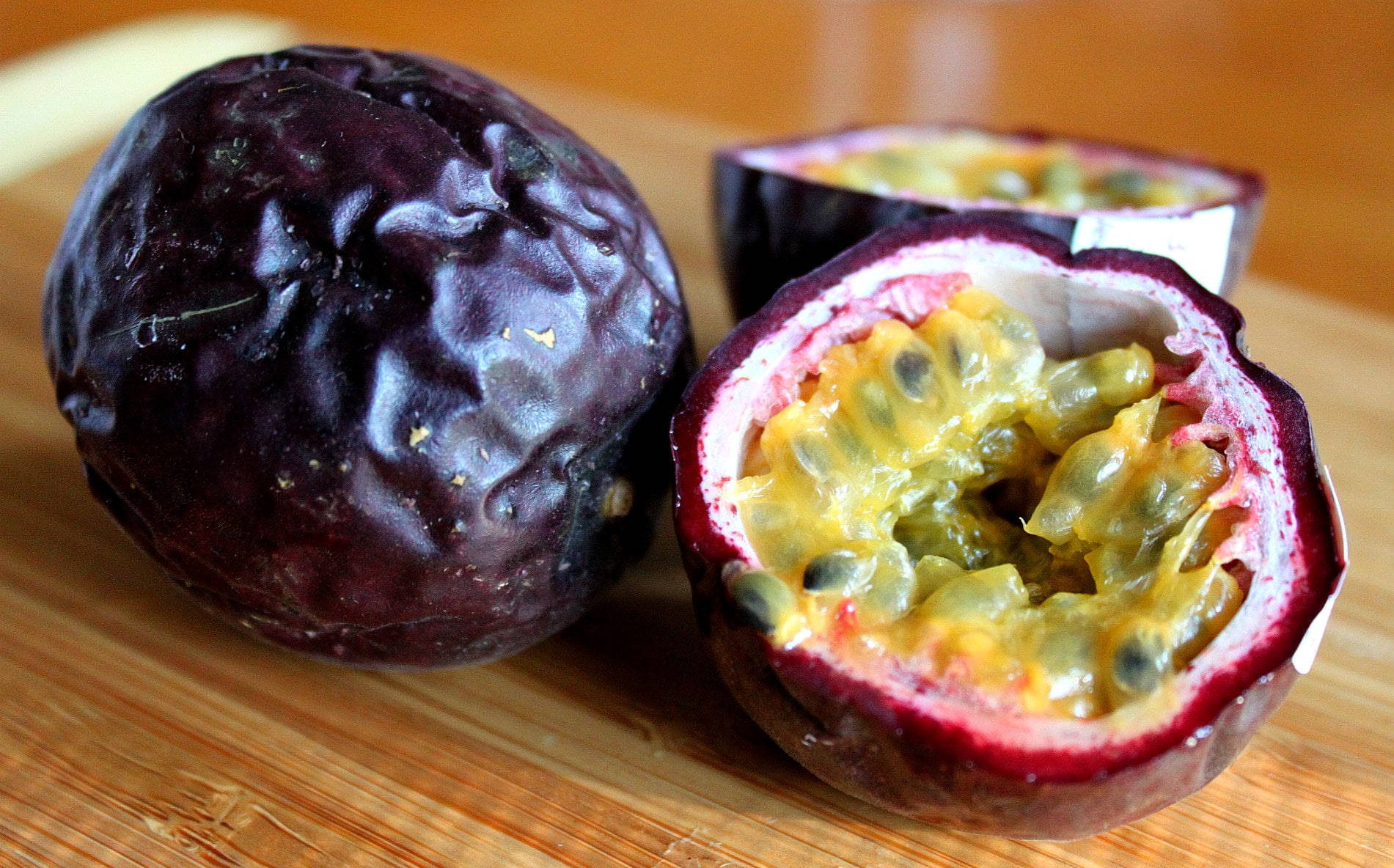 Passion Fruit 桌布 壁紙 — 一個完整的和半切的紫色百香果，在木砧板上露出多汁的黃色果肉和黑色種子。