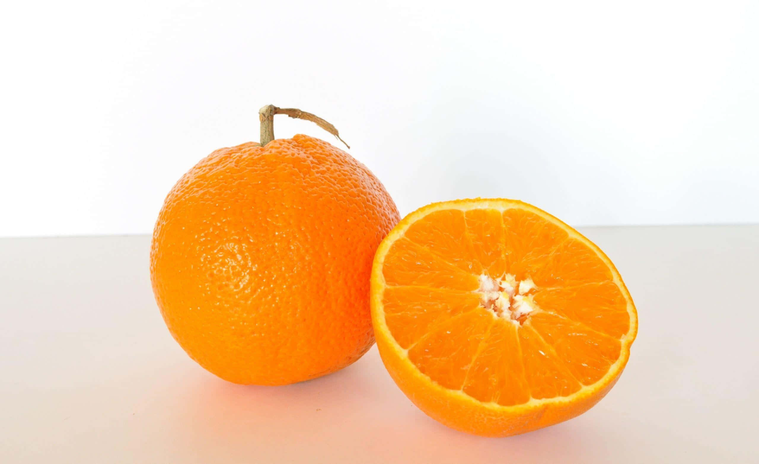 Orange Fruit 桌布 壁紙 — 一個完整的柳橙和半個切開的柳橙，多汁的果肉放在乾淨的白色表面上，在明亮的攝影棚燈光下。