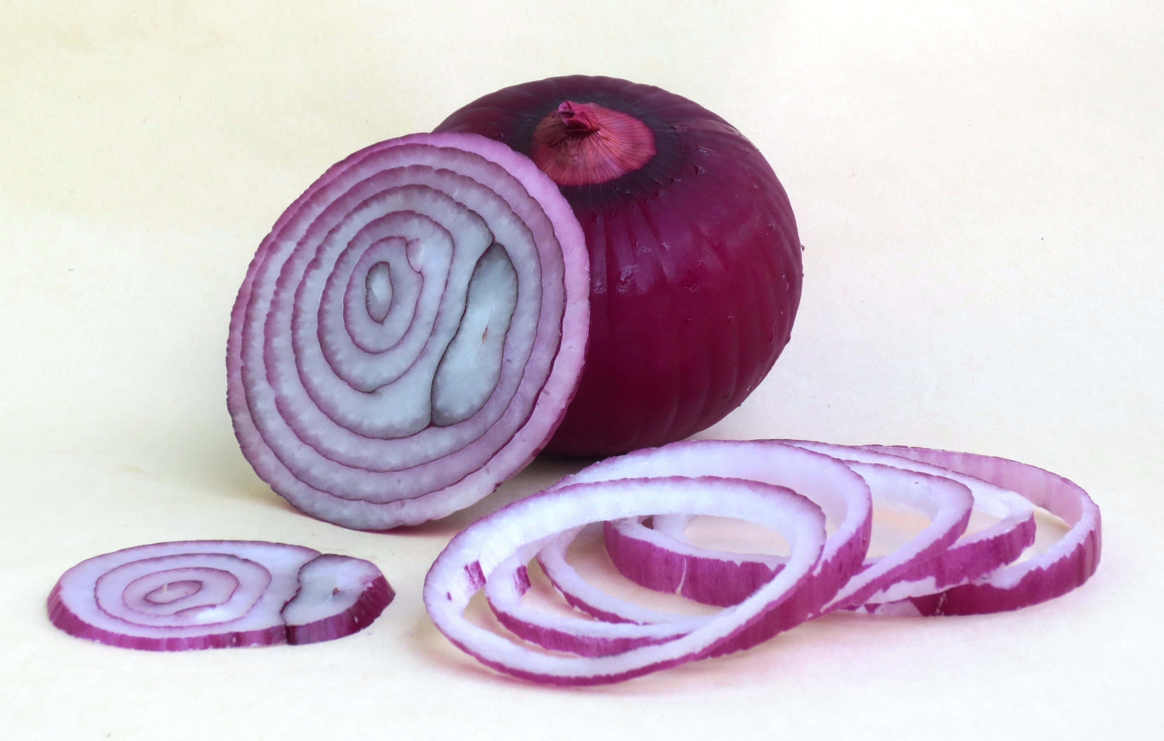 Purple Onions 桌布 壁紙 — 一個完整的紅洋蔥及其切片環在柔和的米色背景上展現出複雜的紫色同心層。