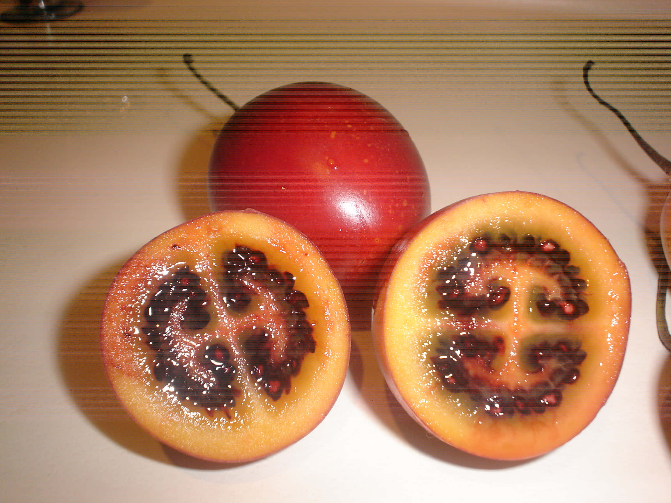 Fruit 桌布 壁紙 — 一個完整的紅色百香果和兩個半邊，露出多汁的橙色果肉和深色種子，放在淺色檯面上。