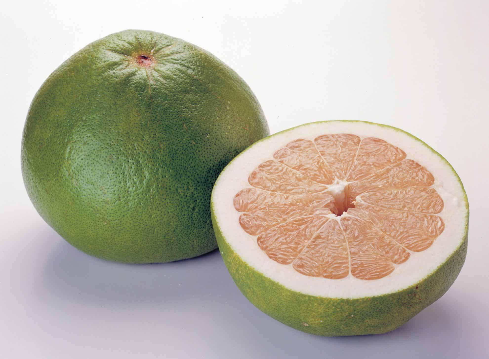 Fruits 桌布 壁紙 — 一個完整的綠色柚子及其一半，露出多汁的粉紅色果肉，背景為潔淨的白色。