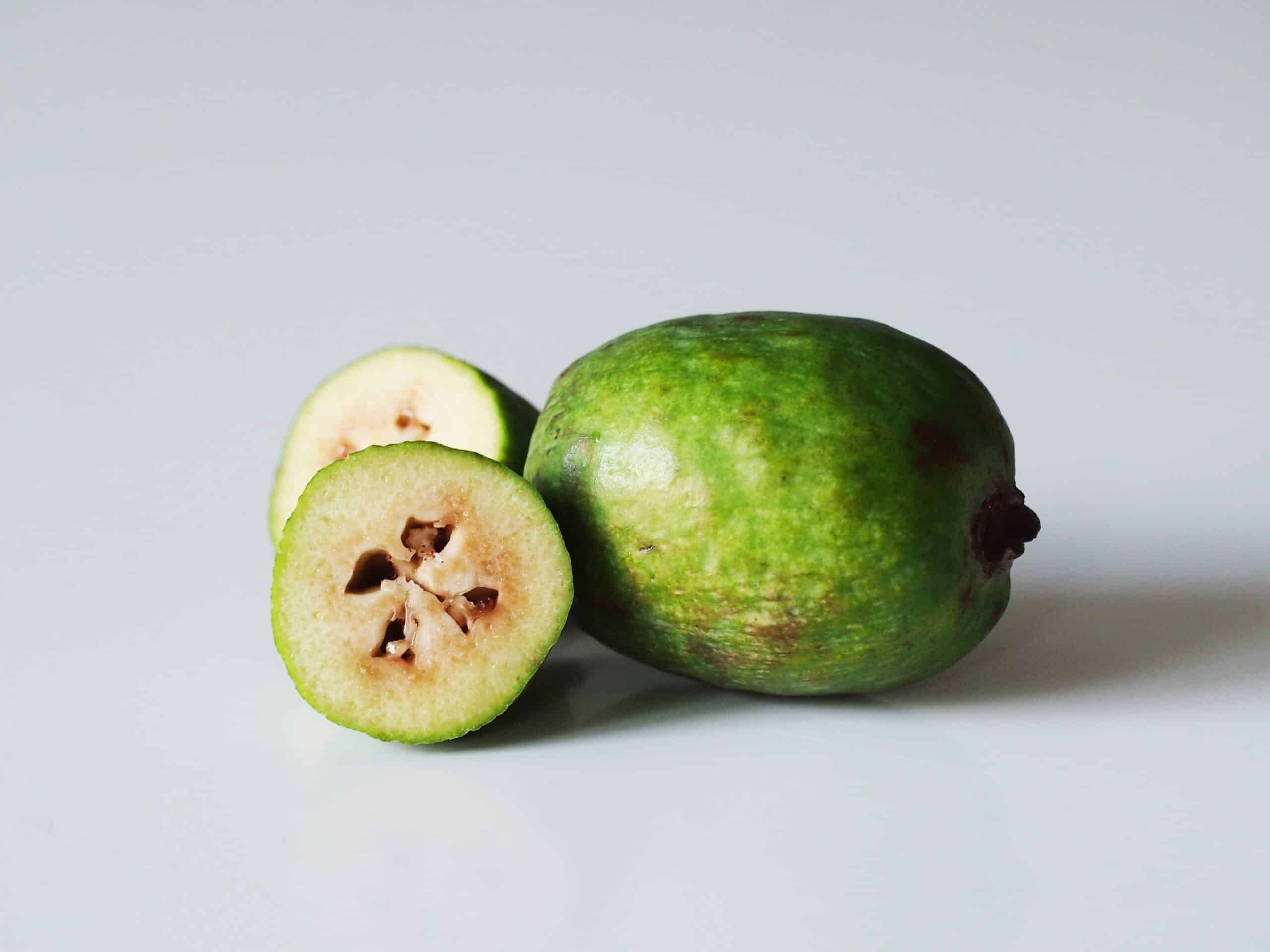 Fruit 桌布 壁紙 — 一個完整的綠色菲油果及其橫切面，在潔白表面上顯露出星形種子。