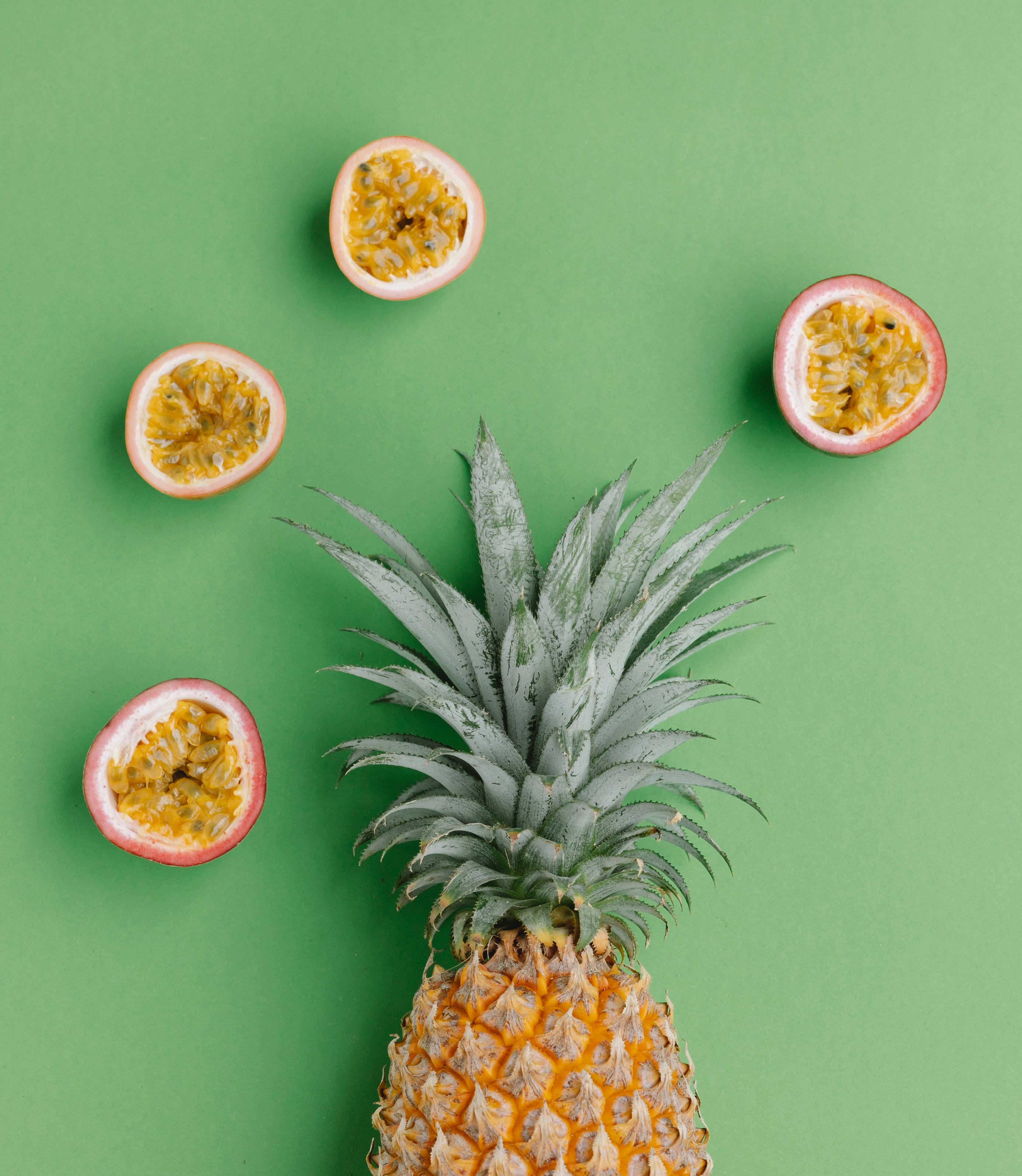 Fruits 桌布 壁紙 — 一個完整的鳳梨，四個切半的百香果圍繞它排列在純綠色背景上。