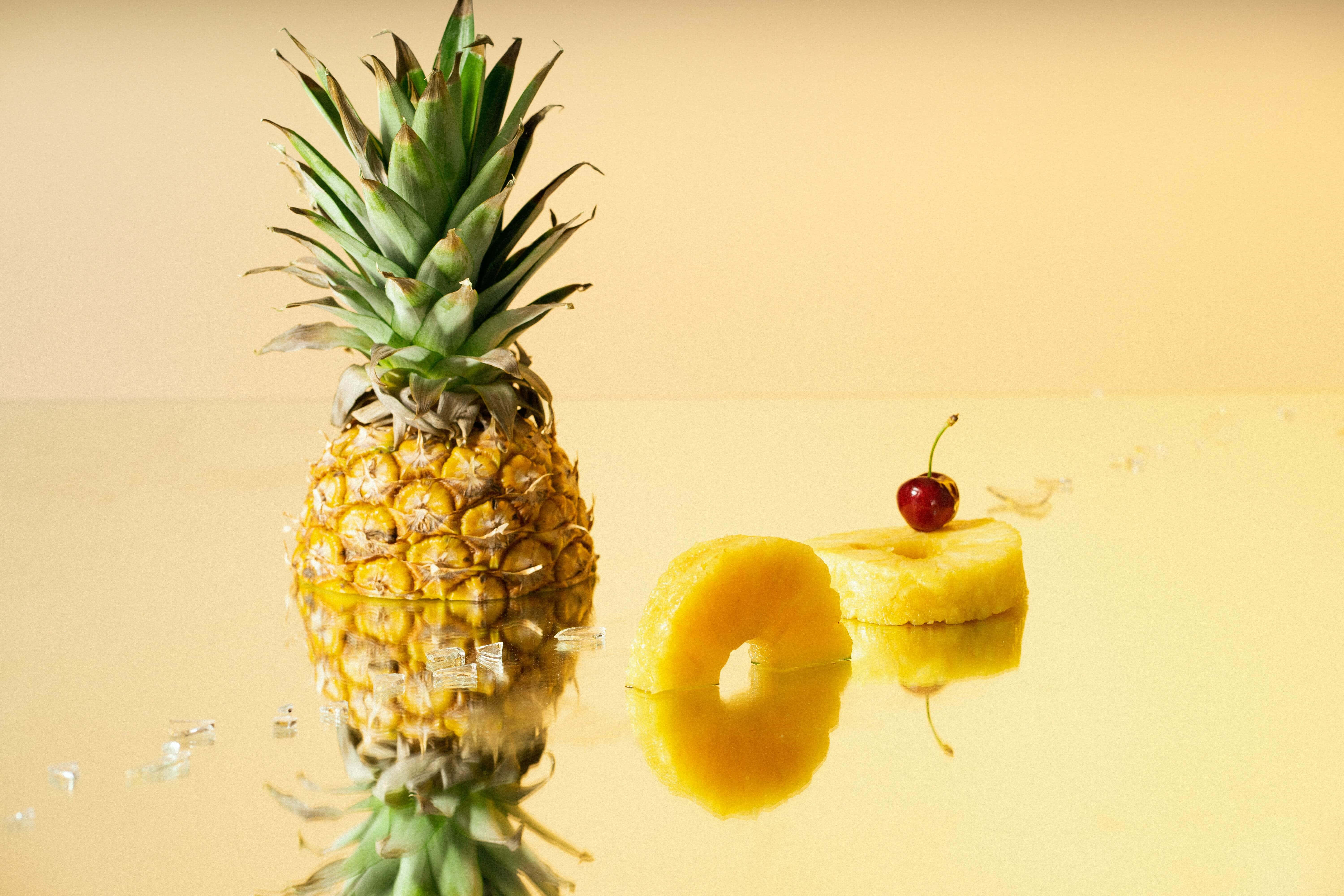 Pineapple 桌布 壁紙 — 一個完整的鳳梨和切片塊，上面放著一顆櫻桃，放在溫暖燈光下的反光金色表面上。