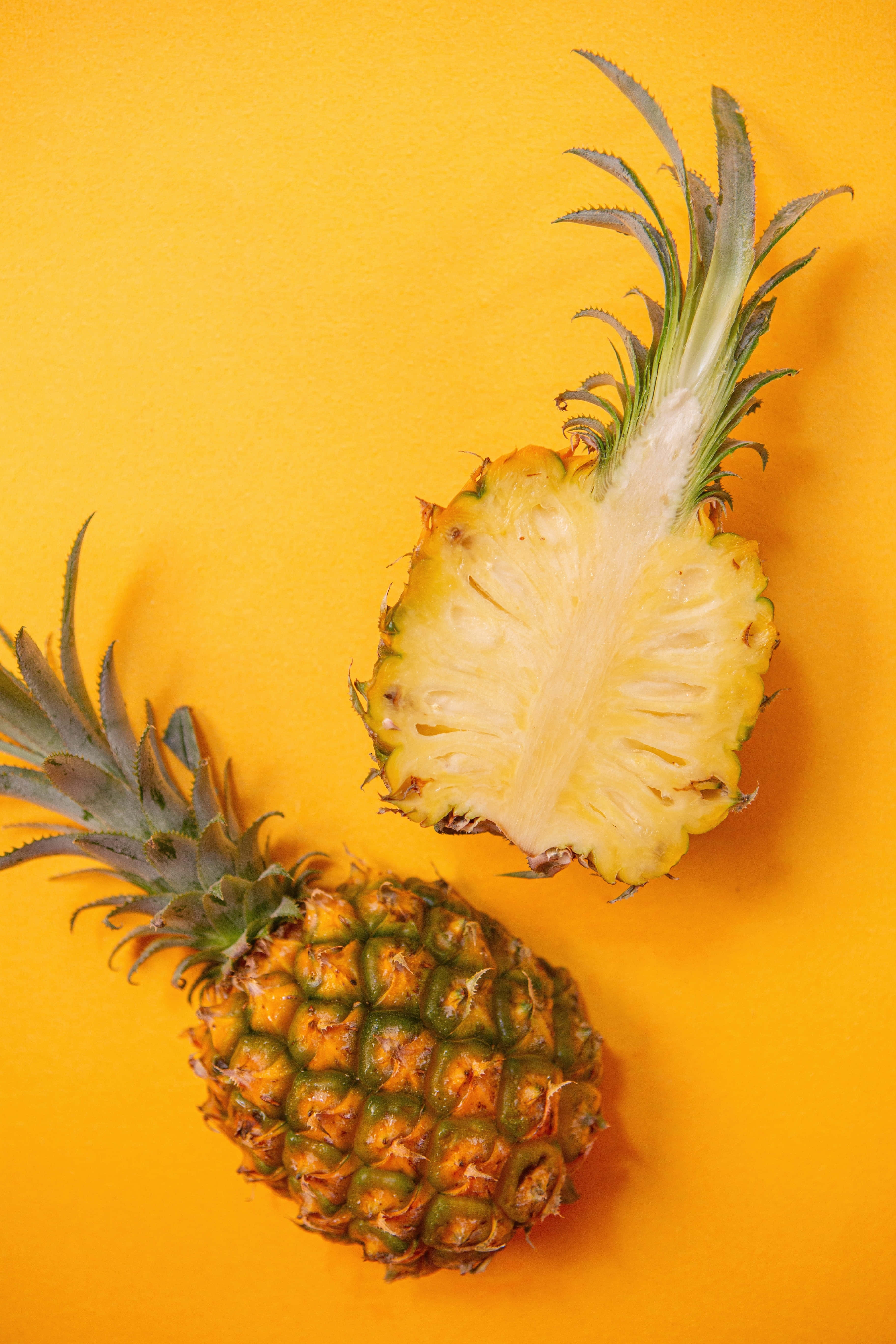 Pineapple 桌布 壁紙 — 一個完整的鳳梨和它的半邊切開部分在鮮黃色背景上展現多汁的果肉。