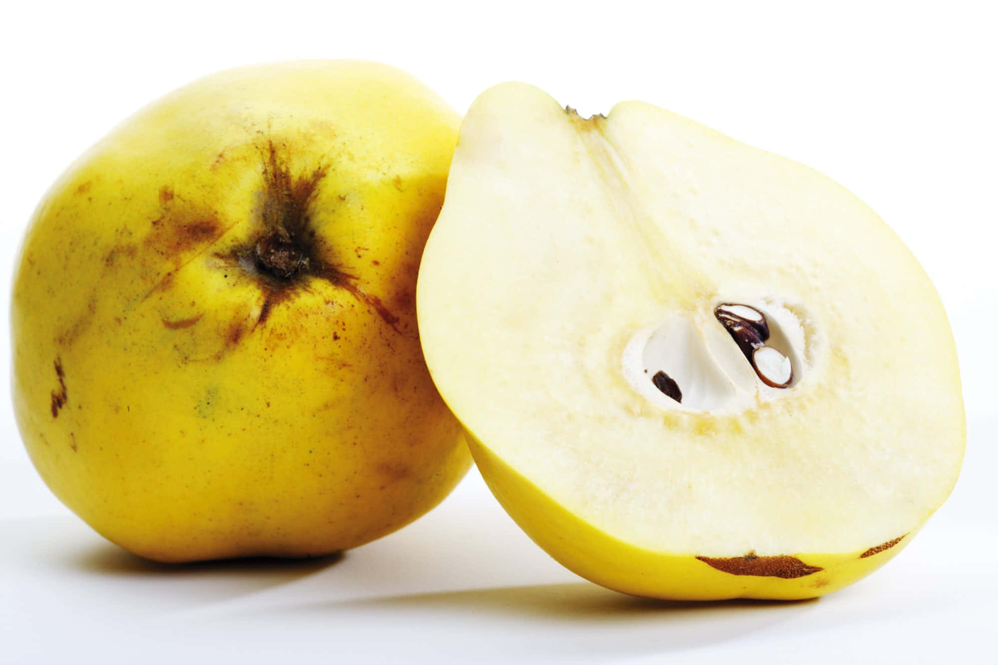Quince 桌布 壁紙 — 一個完整的黃色榲桲旁邊是一個切半的榲桲，露出淡色果肉和深色種子，背景為純白色。