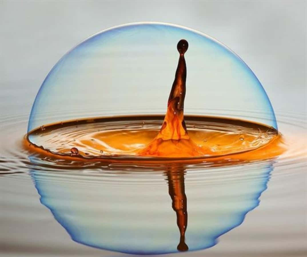 Water Drop 桌布 壁紙 — 一個完美的藍色氣泡懸浮在琥珀色液體上方，一滴水滴以慢動作升起，下方有它的倒影。