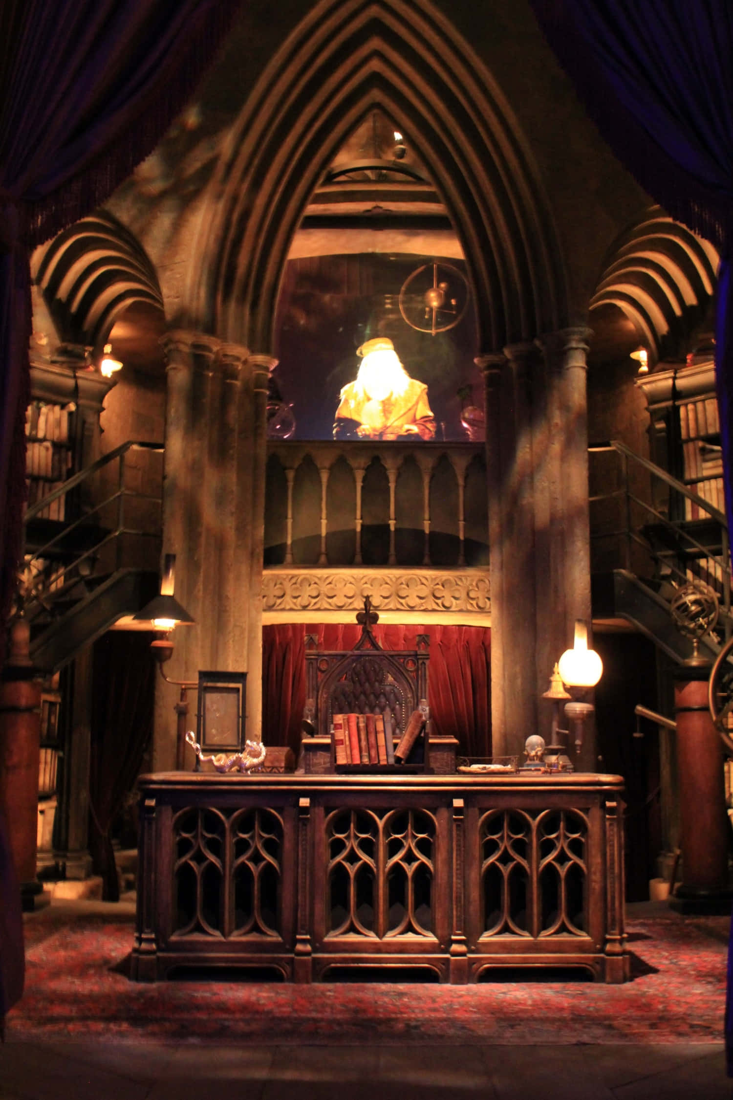 The Hogwarts Headmaster's Office 桌布 壁紙 — 一個宏偉的哥德式書房，配有木桌、紅色地毯，以及在拱形石窗下發光的半身像。