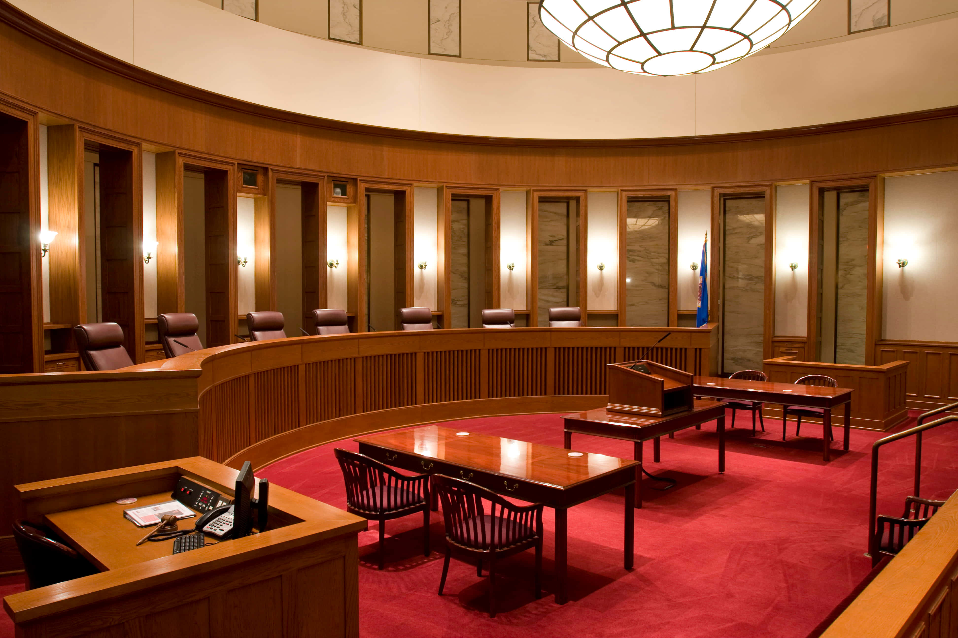 Courtroom 桌布 壁紙 — 一個宏偉的圓形法庭，配有豐富的木鑲板、紅色地毯和一個位於大型吊燈下的中央法官席。