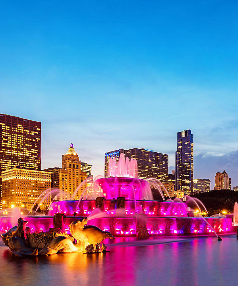 Illinois 桌布 壁紙 — 一個宏偉的城市噴泉沐浴在充滿活力的粉紅色燈光中，映襯著暮色城市天際線和發光的摩天大樓。
