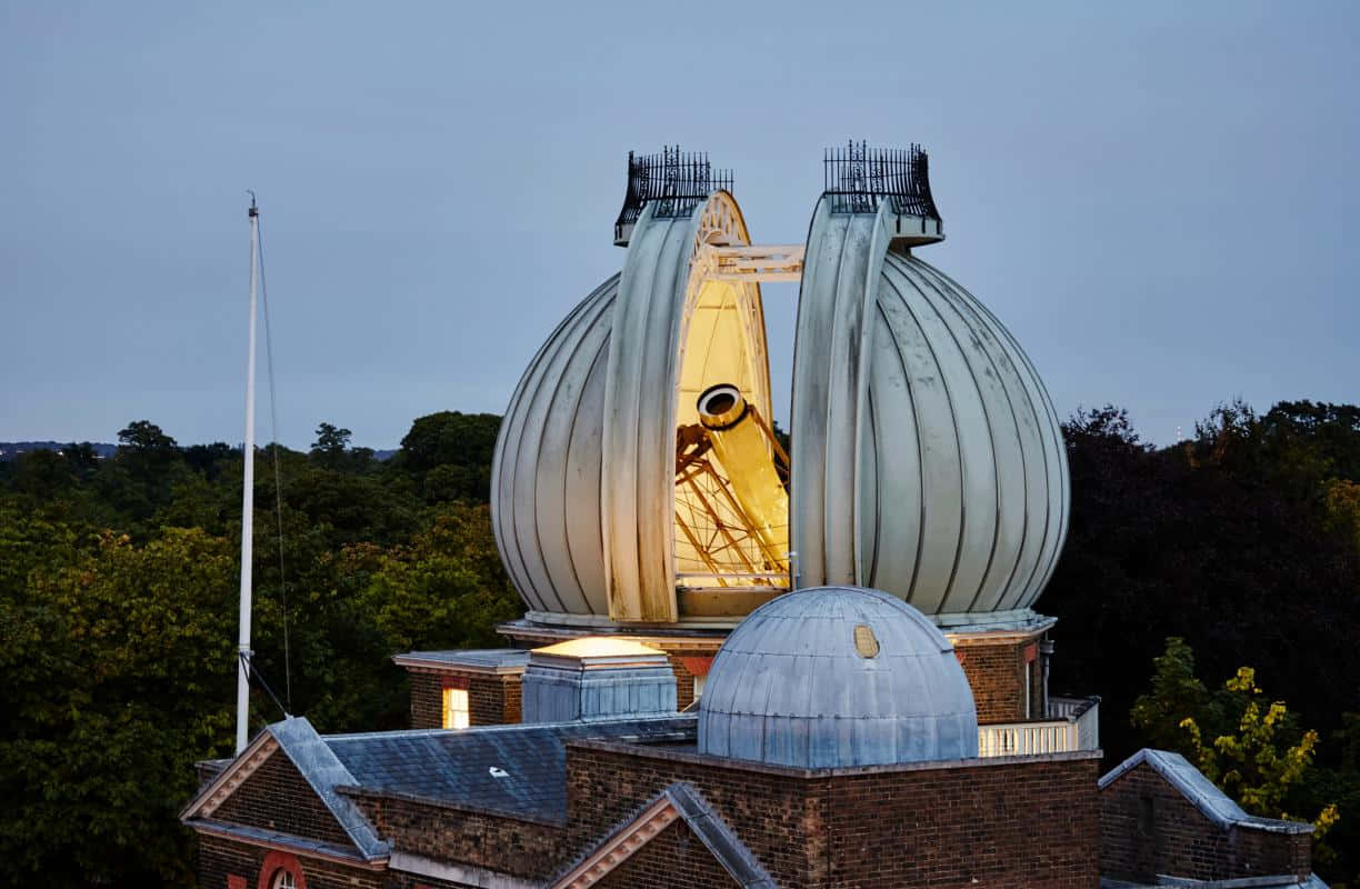 Observatory 桌布 壁紙 — 一個宏偉的天文台圓頂溫暖地發光，其兩半打開，在暮色天空中顯露出一個巨大的望遠鏡。