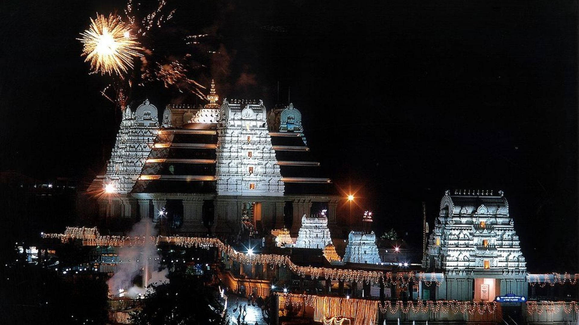 Bangalore 桌布 壁紙 — 一個宏偉的寺廟建築群在夜晚被照亮，煙火在其複雜的塔樓上方爆炸。