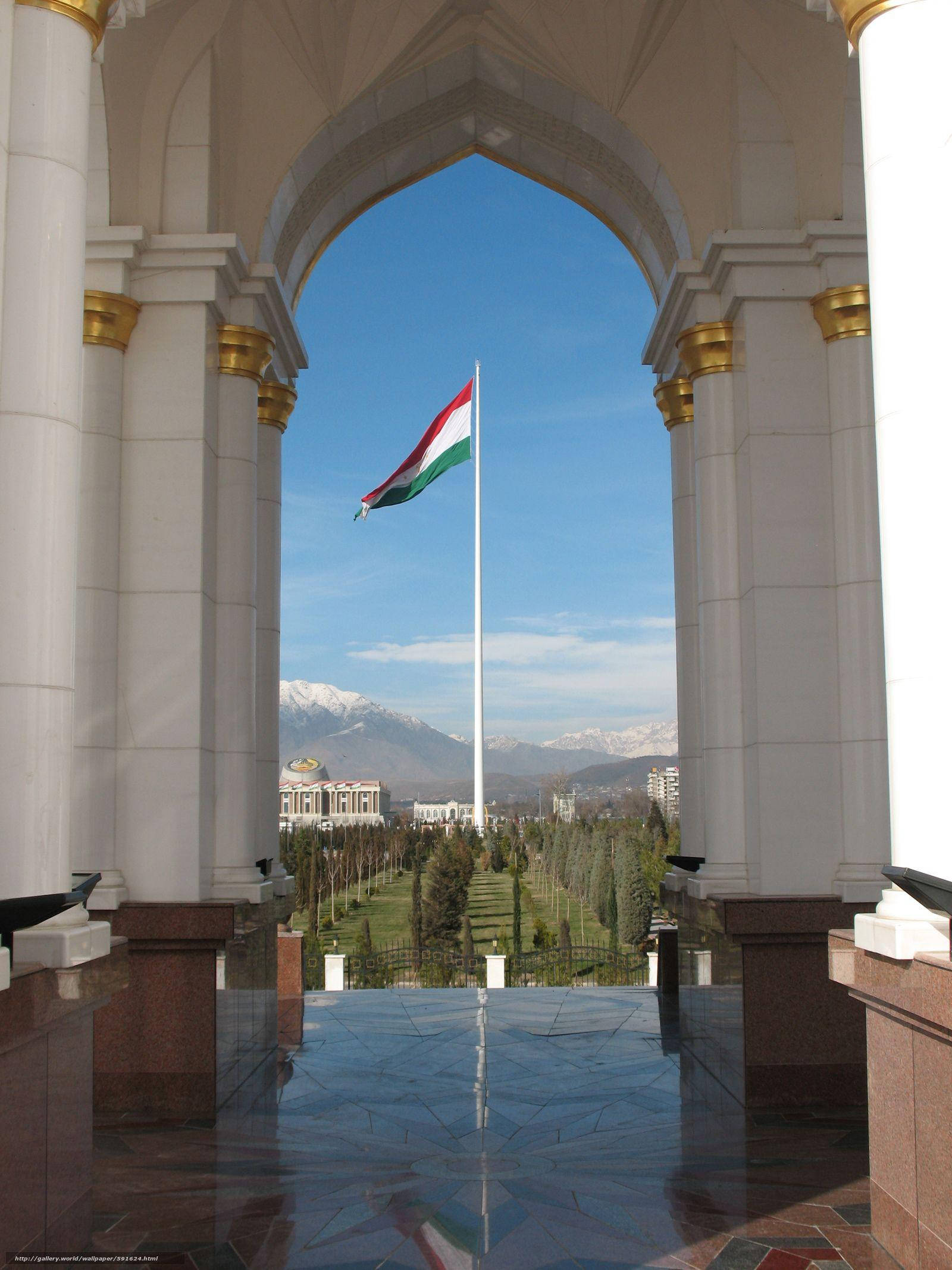 Tajikistan 桌布 壁紙 — 一個宏偉的拱形入口框住了一面在晴朗藍天和遠處雪山背景下飄揚的國旗。
