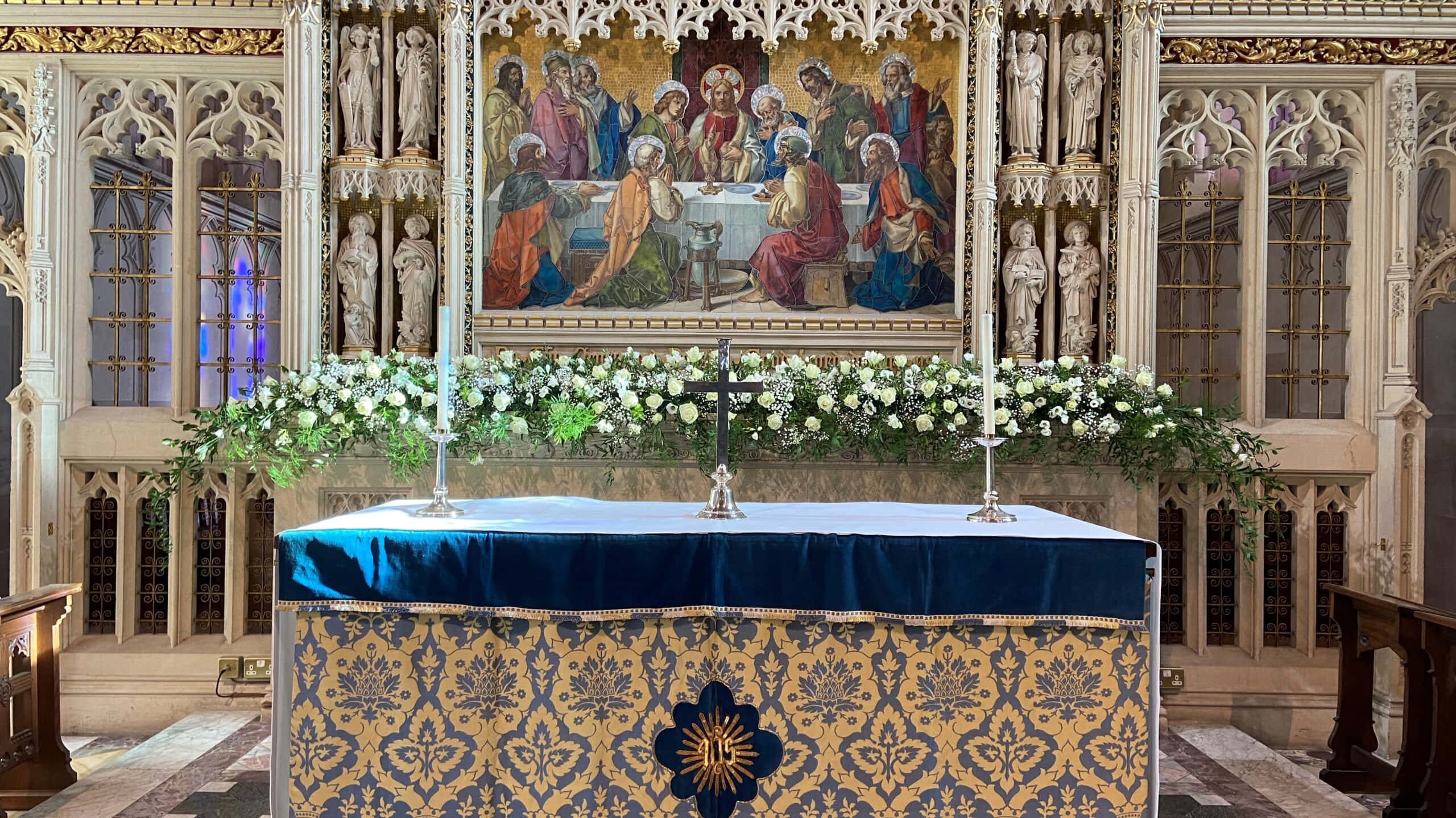 Catholic 桌布 壁紙 — 一個宏偉的教堂祭壇，裝飾著白色鮮花和藍色錦緞布，下方是充滿活力的宗教壁畫。