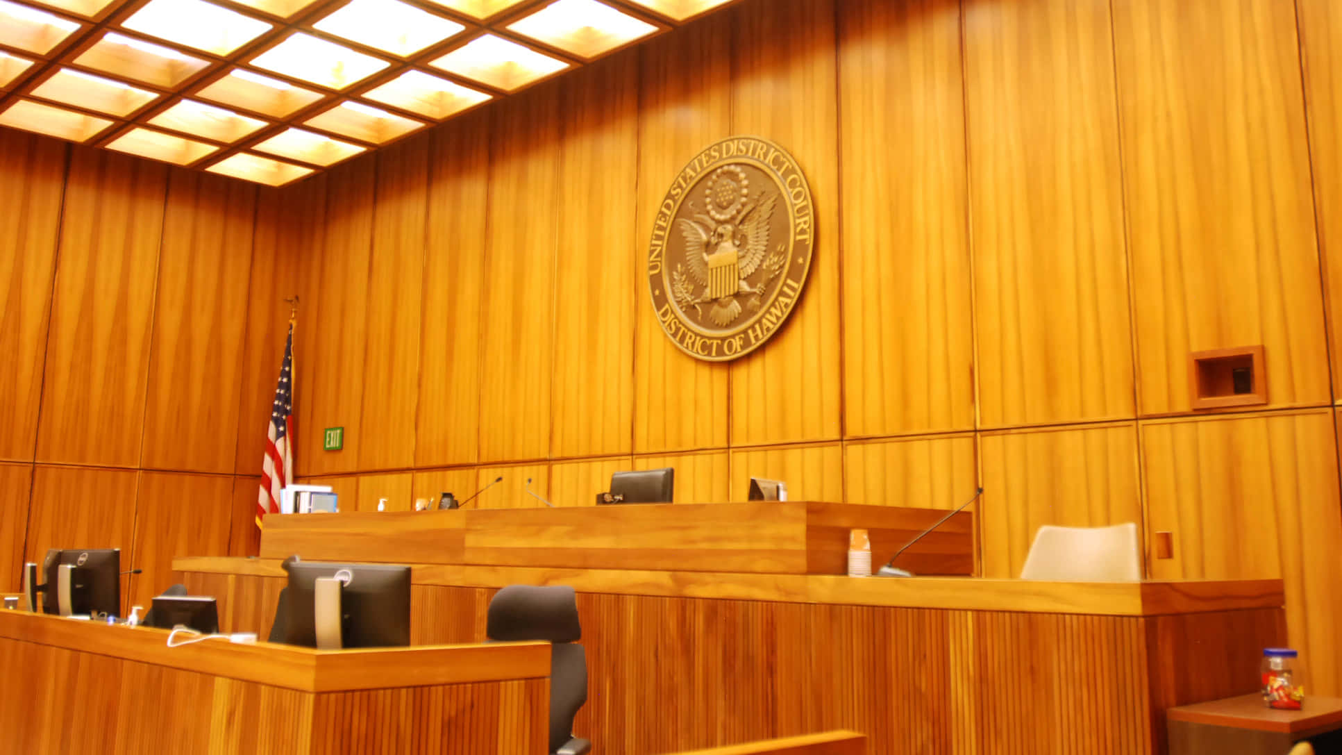 Courtroom 桌布 壁紙 — 一個宏偉的木製法庭，牆上掛有大型美國聯邦地區法院印章，並豎立著美國國旗。