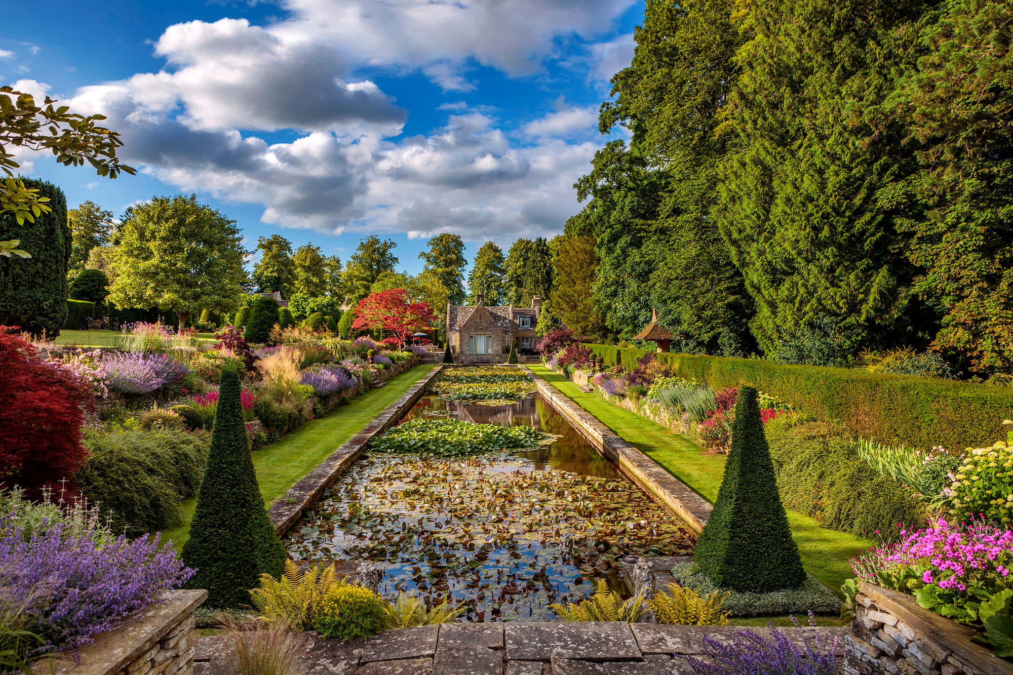 Garden Photography 桌布 壁紙 — 一個宏偉的正式花園，設有長長的水景，兩旁是修剪整齊的樹籬和色彩繽紛的花朵，在晴朗的藍天白雲下。