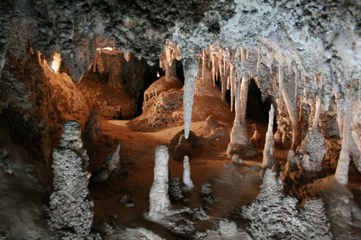 Cave 桌布 壁紙 — 一個宏偉的洞穴，被溫暖的燈光照亮，展示著高聳的鐘乳石和石筍，呈現大地色調。