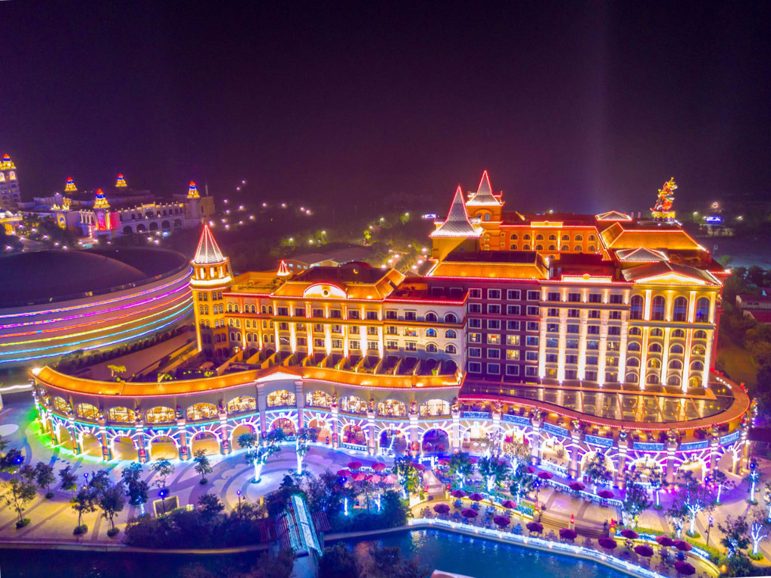 Guangzhou 桌布 壁紙 — 一個宏偉的照明度假村綜合體在夜間散發出鮮豔的光芒，色彩繽紛的燈光勾勒出其華麗的建築和周圍的水景。