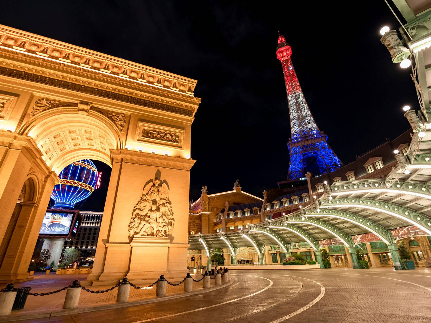 Paris Las Vegas 桌布 壁紙 — 一個宏偉的照明拱門框住了一個複製的艾菲爾鐵塔，在黑暗的夜空中閃爍著紅色和藍色。