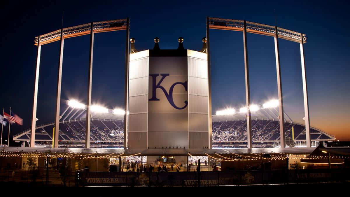 Kansas 桌布 壁紙 — 一個宏偉的照明體育場在黃昏時分，中央塔樓上閃爍著「KC」標誌，背景是深藍色的天空。