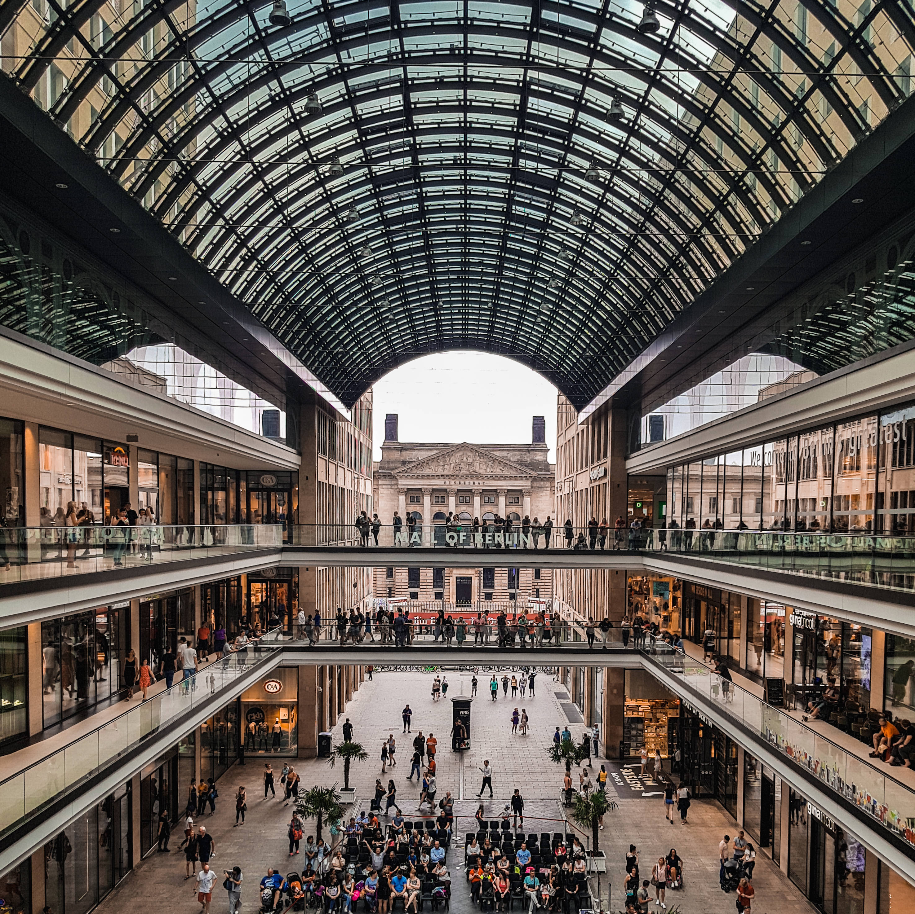Berlin 桌布 壁紙 — 一個宏偉的玻璃圓頂購物拱廊，多層購物者和商店櫥窗在彎曲的透明屋頂下。