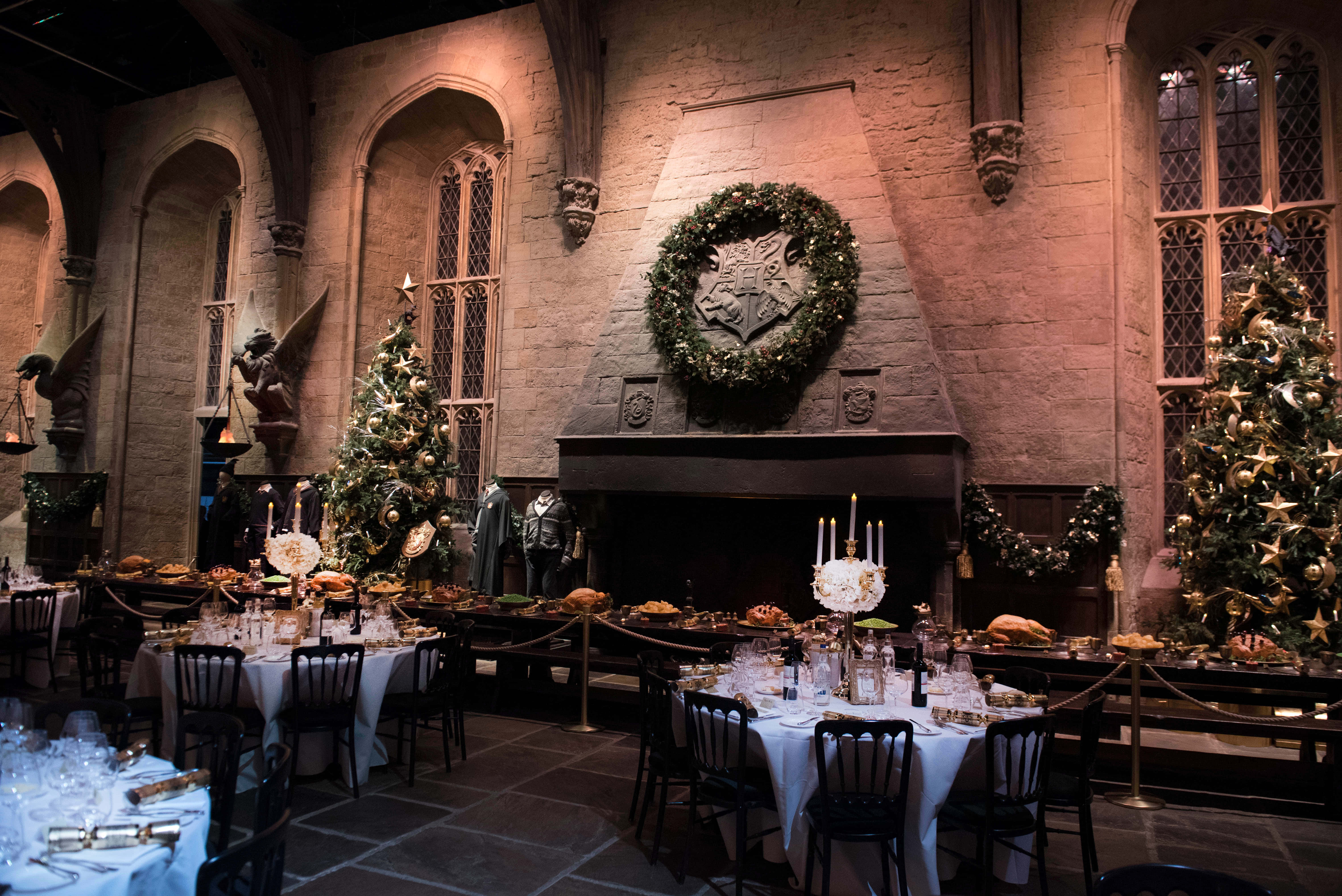 Harry Potter Christmas 桌布 壁紙 — 一個宏偉的石廳，裝飾著聖誕樹和節日花環，在溫暖的燭光下準備了一場豐盛的節日盛宴。