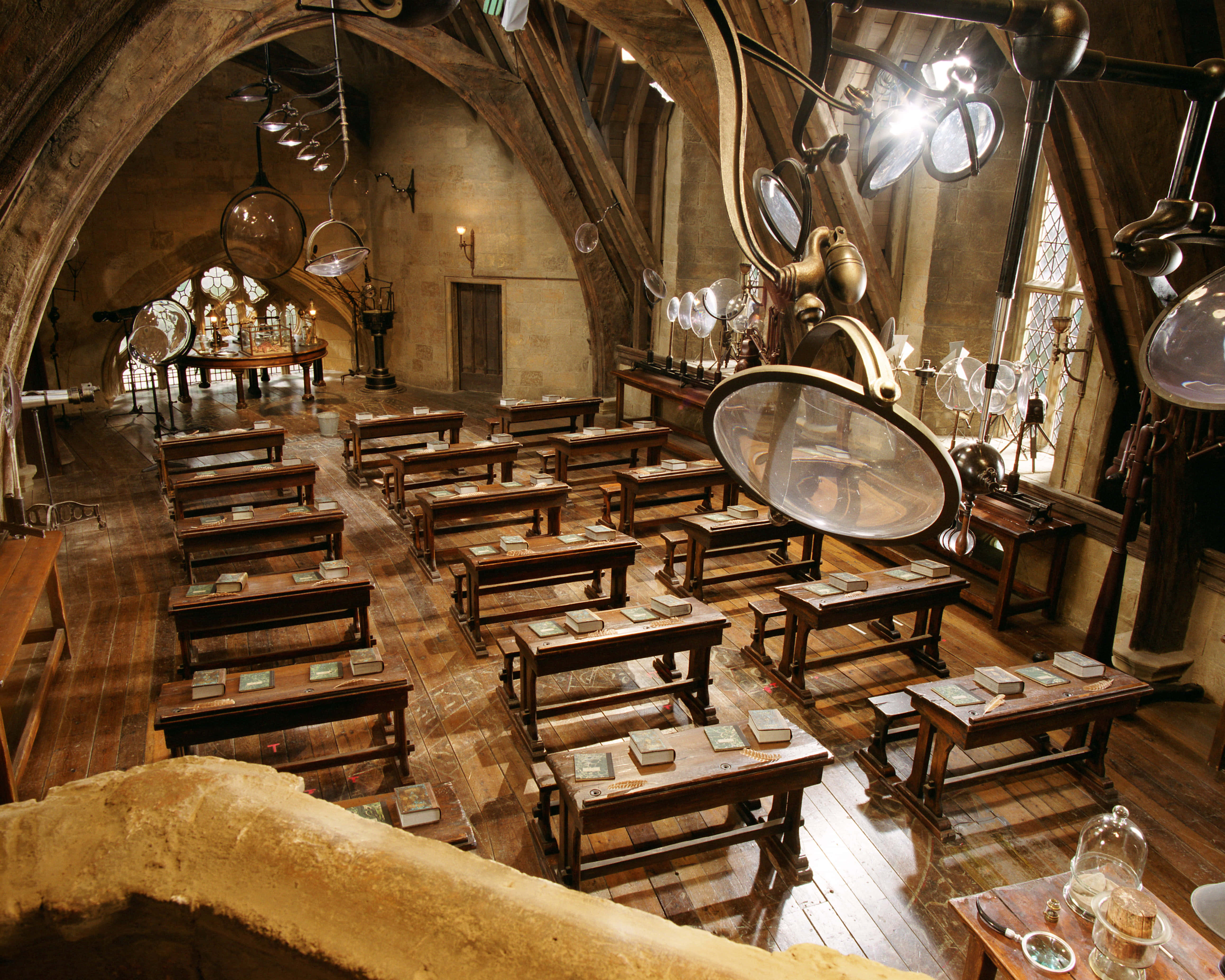 The Hogwarts Potions Class 桌布 壁紙 — 一個宏偉的石牆教室，充滿木製書桌、書籍和漂浮的玻璃地球儀，在溫暖的燈光下。