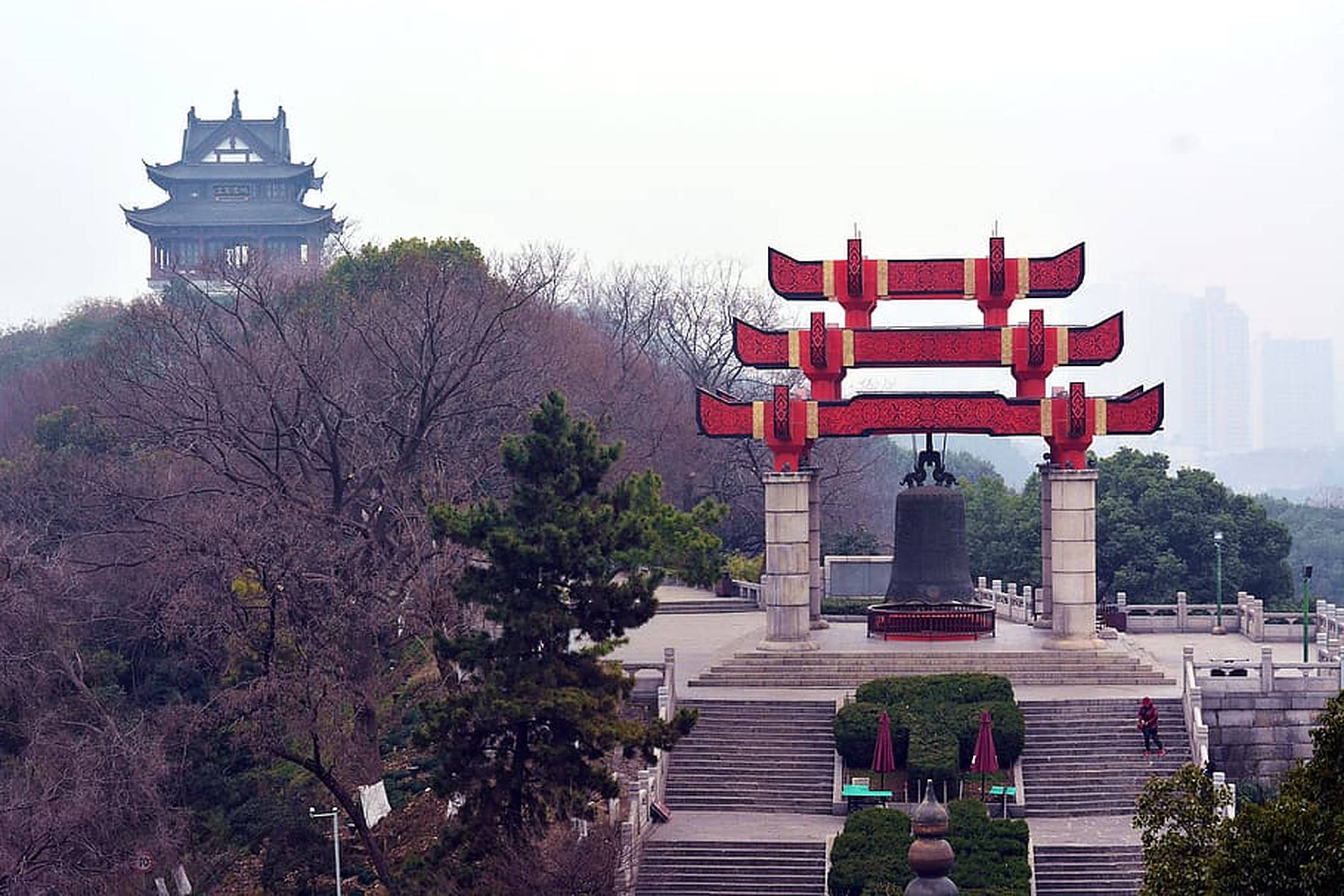 Wuhan 桌布 壁紙 — 一個宏偉的紅色傳統拱門框住了一個大鐘，鐘放在石階上，背景是霧氣瀰漫的山丘上的寶塔。
