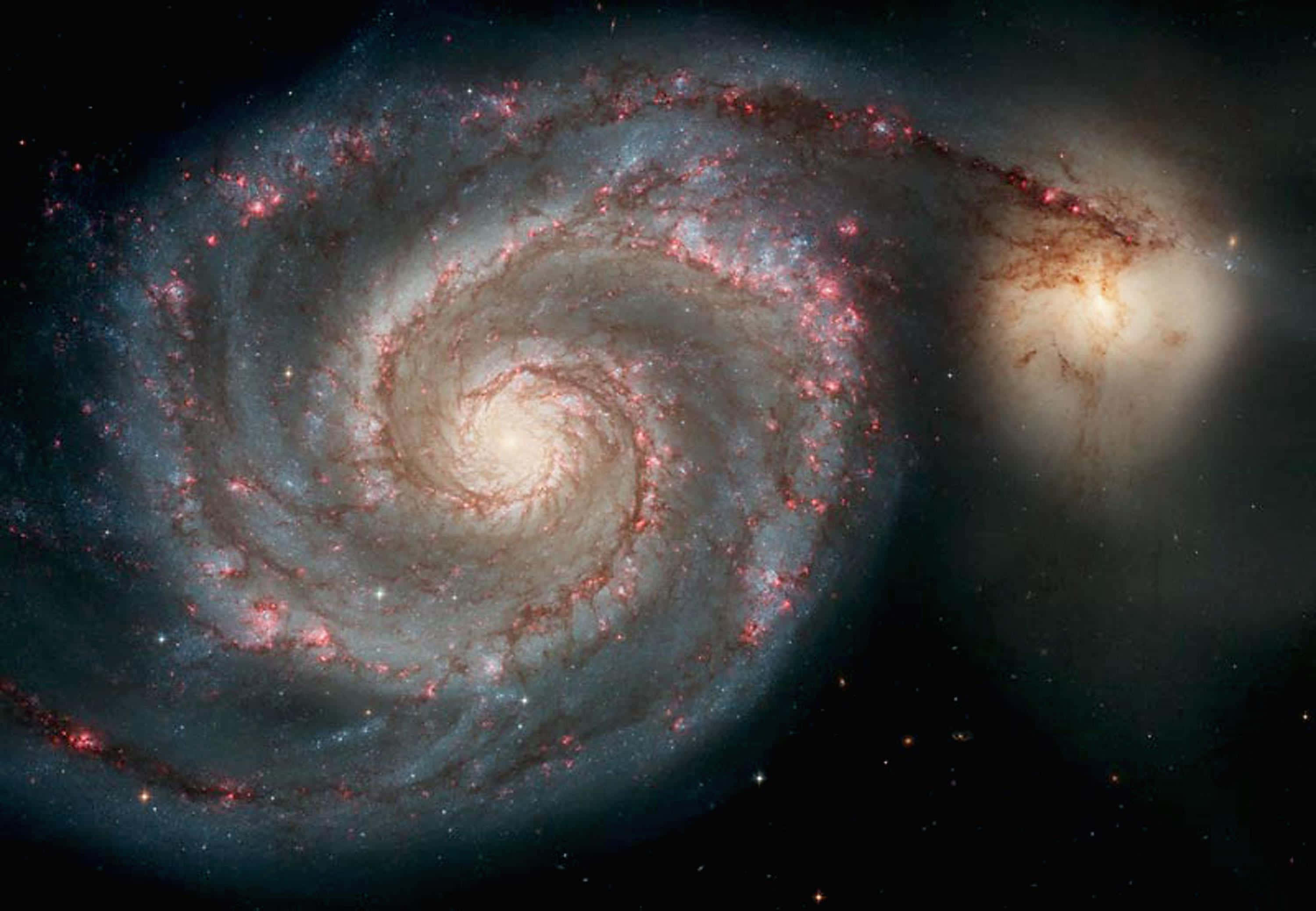 Nasa Galaxy 桌布 壁紙 — 一個宏偉的螺旋星系在繁星點點的宇宙虛空中旋轉，伴隨著發光的紅色恆星和藍色塵埃帶。
