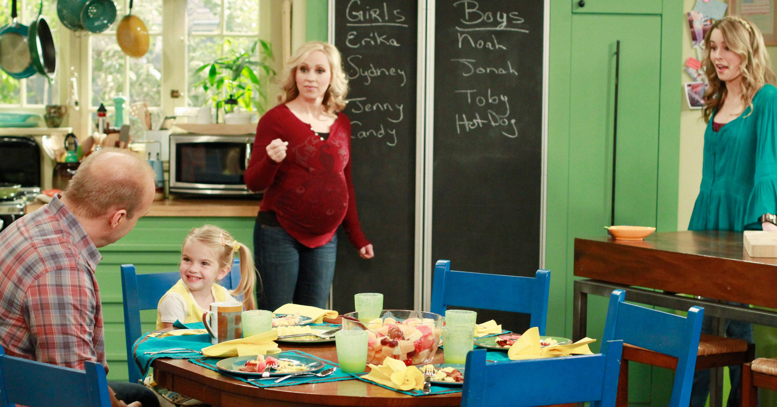 Good Luck Charlie 桌布 壁紙 — 一個家庭圍繞著一張色彩繽紛的餐桌，在一個明亮的廚房裡，黑板牆上列出了孩子們的名字。