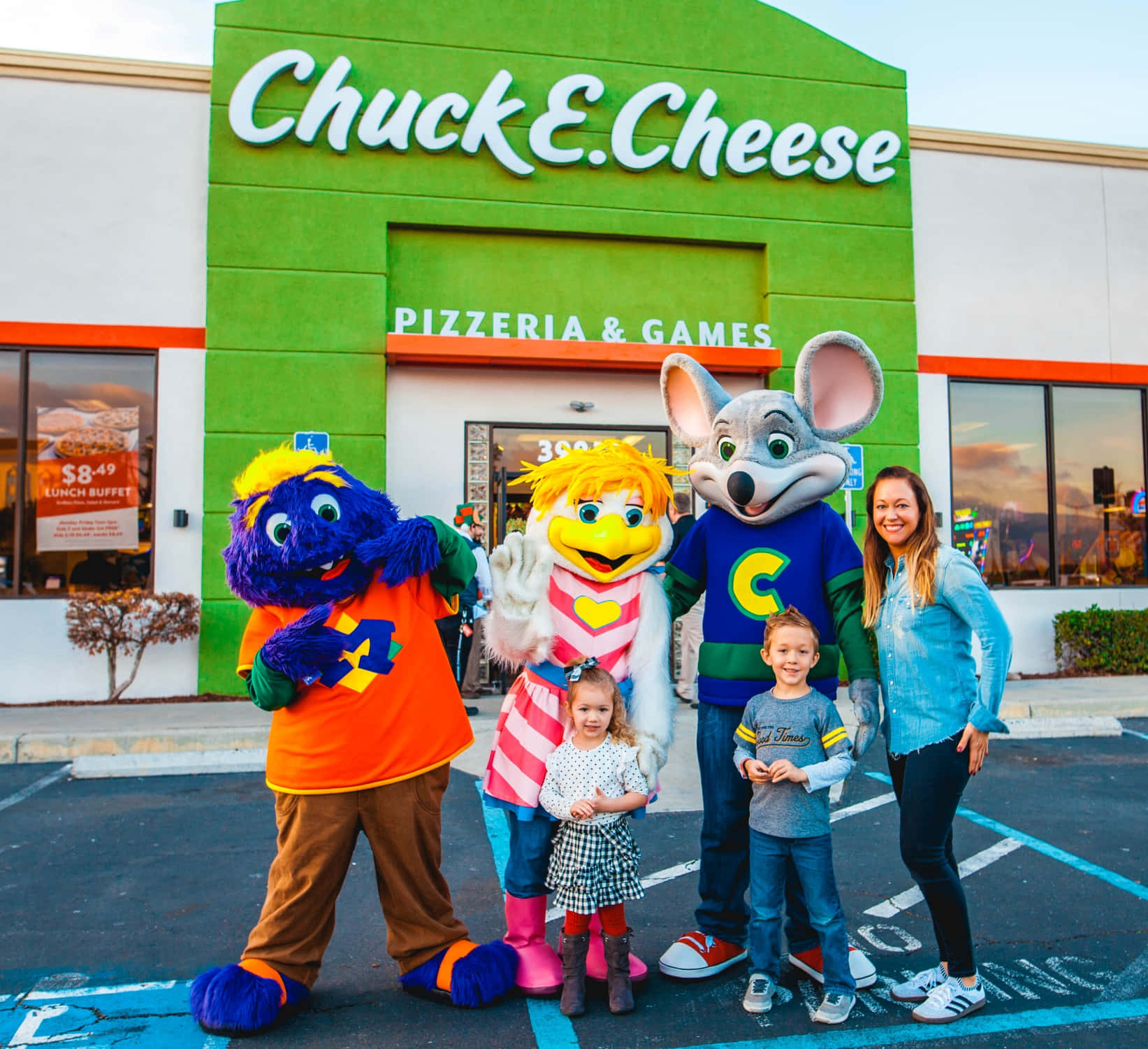 查克芝士 桌布 壁紙 — 一個家庭在日落時分與三個Chuck E. Cheese吉祥物在明亮的綠色披薩店前合影。