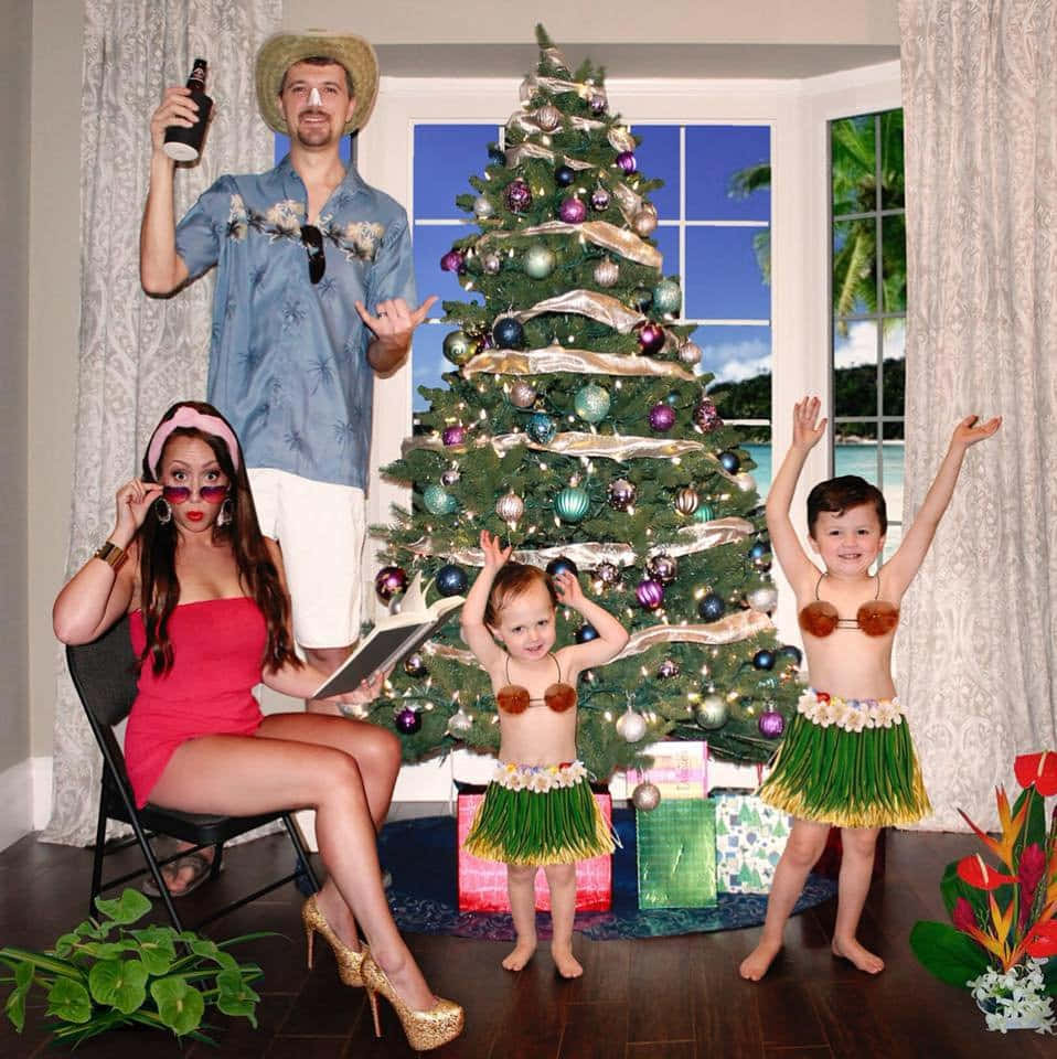 Family 桌布 壁紙 — 一個家庭穿著熱帶服裝，在裝飾好的聖誕樹周圍愉快地擺姿勢，窗外可以看到海灘景色。
