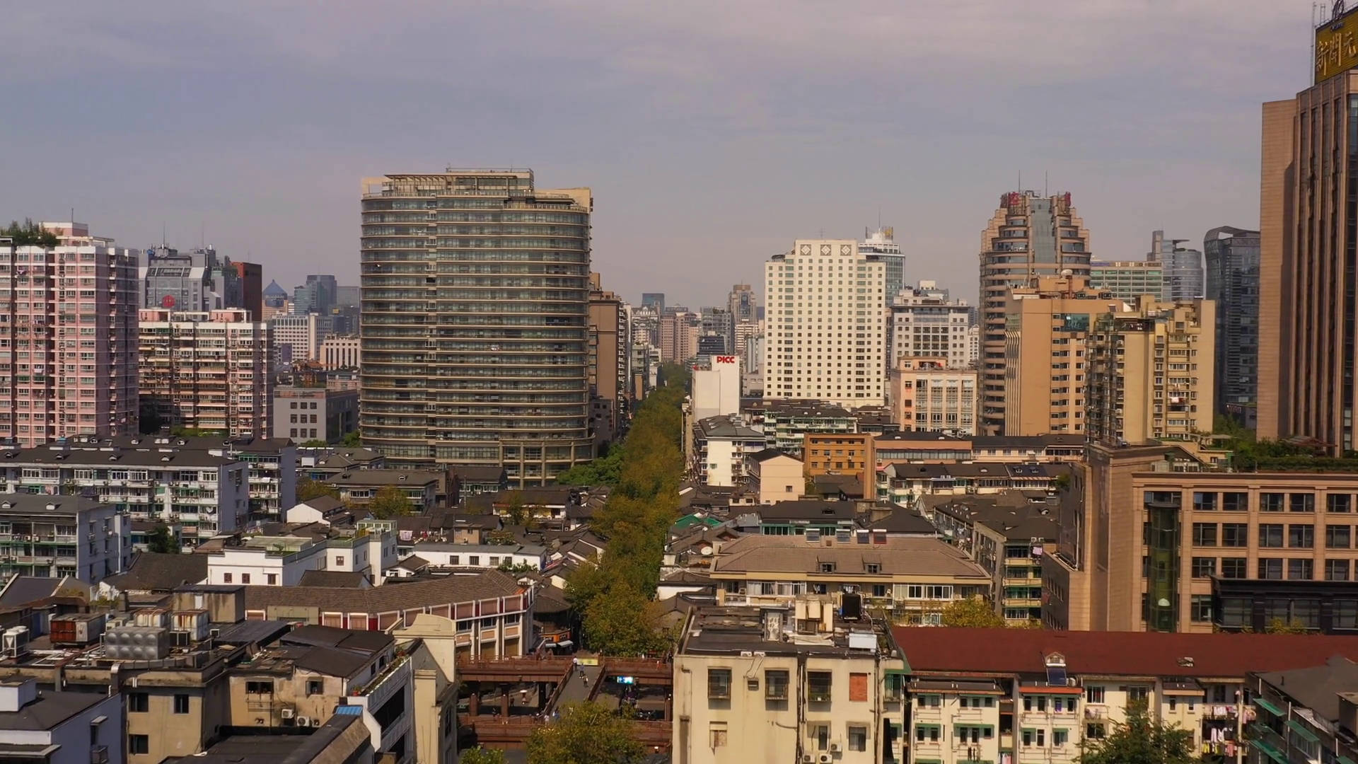 Hangzhou 桌布 壁紙 — 一個密集城市天際線的全景視圖，現代玻璃塔在朦朧天空下聳立於傳統低層建築之上。