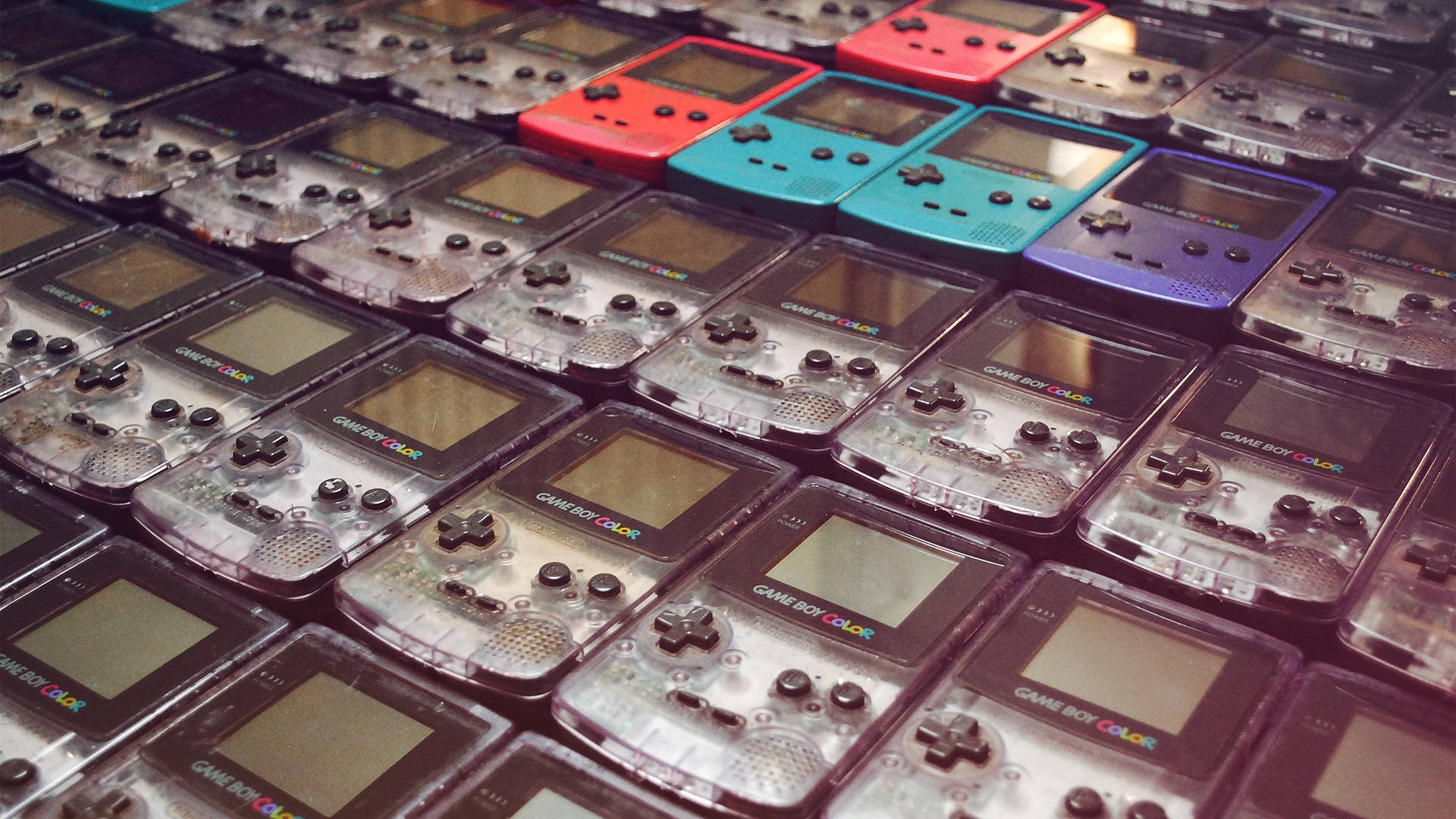 game 桌布 壁紙 — 一個密集的網格，裡面是透明塑膠盒中的 Game Boy Color 掌上遊戲機，紅色、藍色和紫色的主機特別突出。