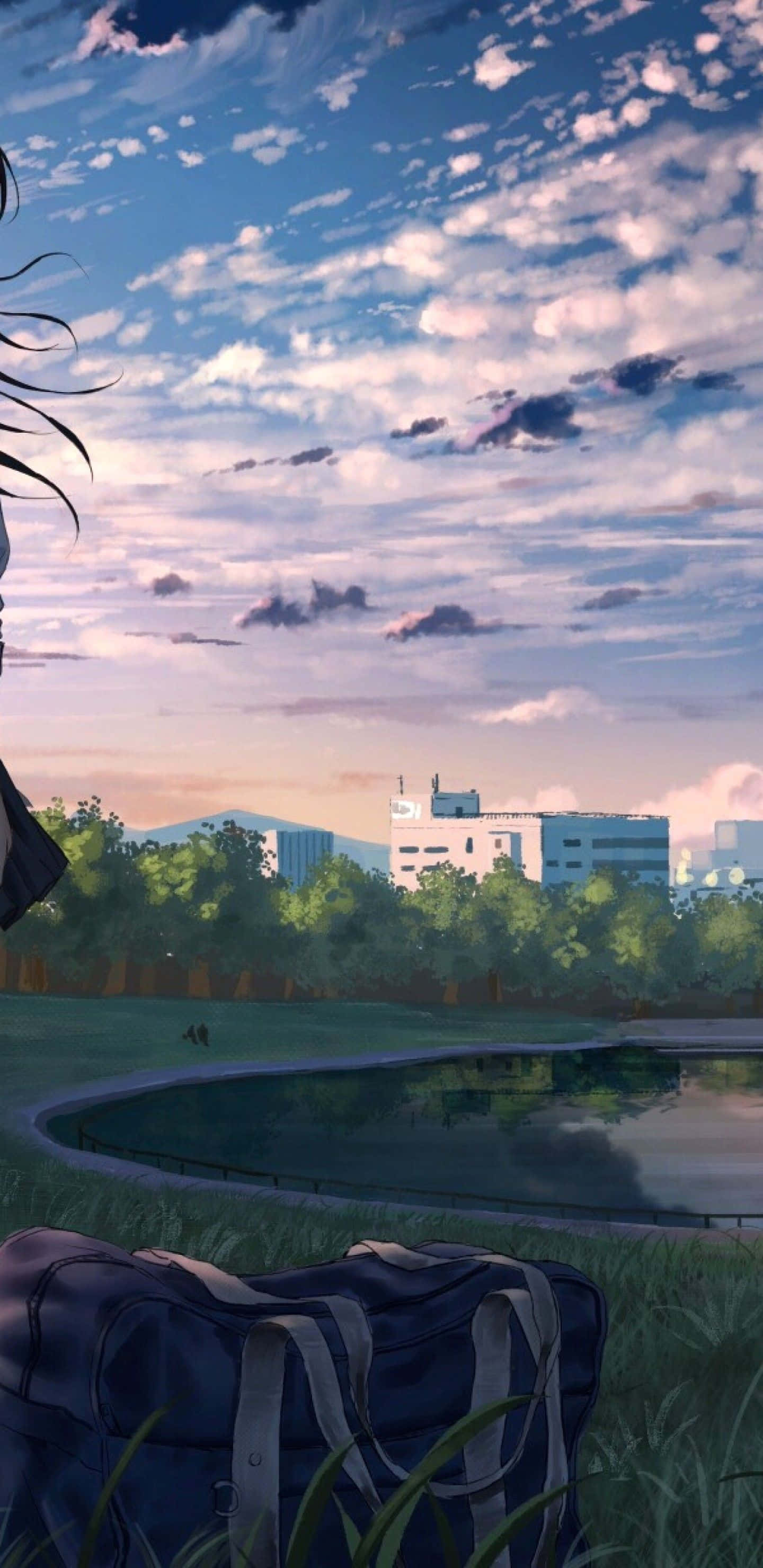 Anime Park Scenery 桌布 壁紙 — 一個寧靜的動漫風格場景，草地上有一個藍色行李袋，俯瞰池塘和遠處的建築物，天空柔和暮色。