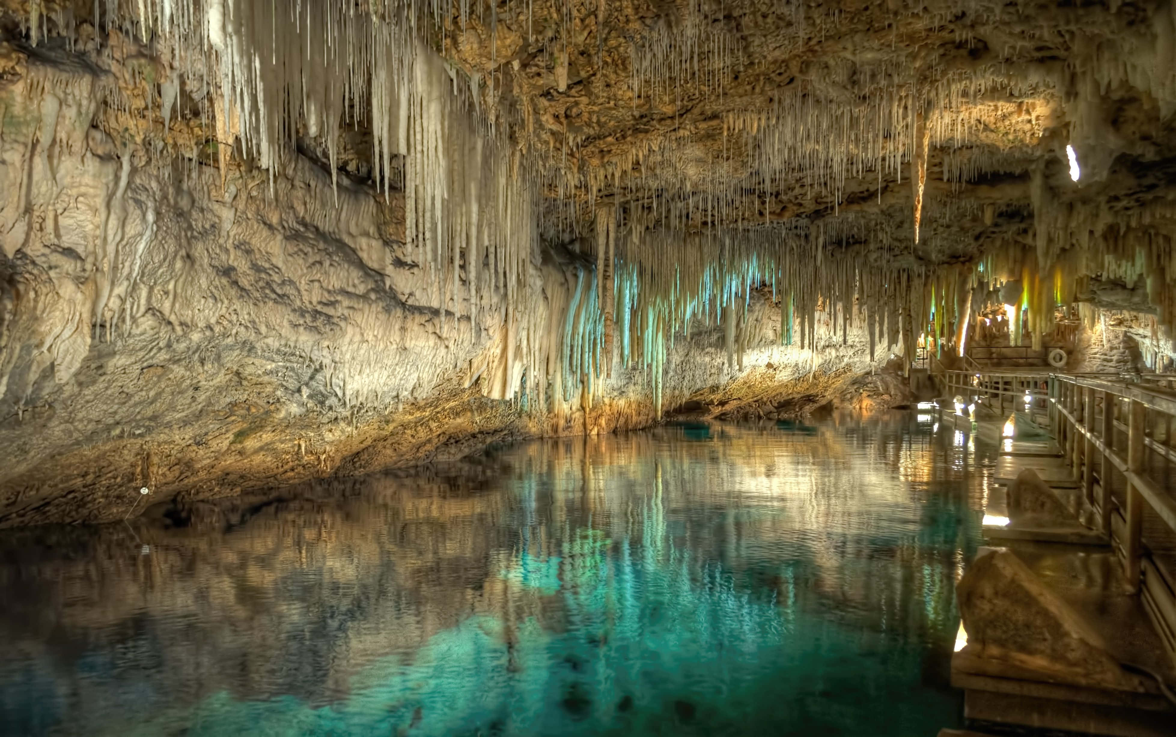 Cave 桌布 壁紙 — 一個寧靜的地下洞穴，碧綠色的水面倒映著發光的鐘乳石和一條木製步道。
