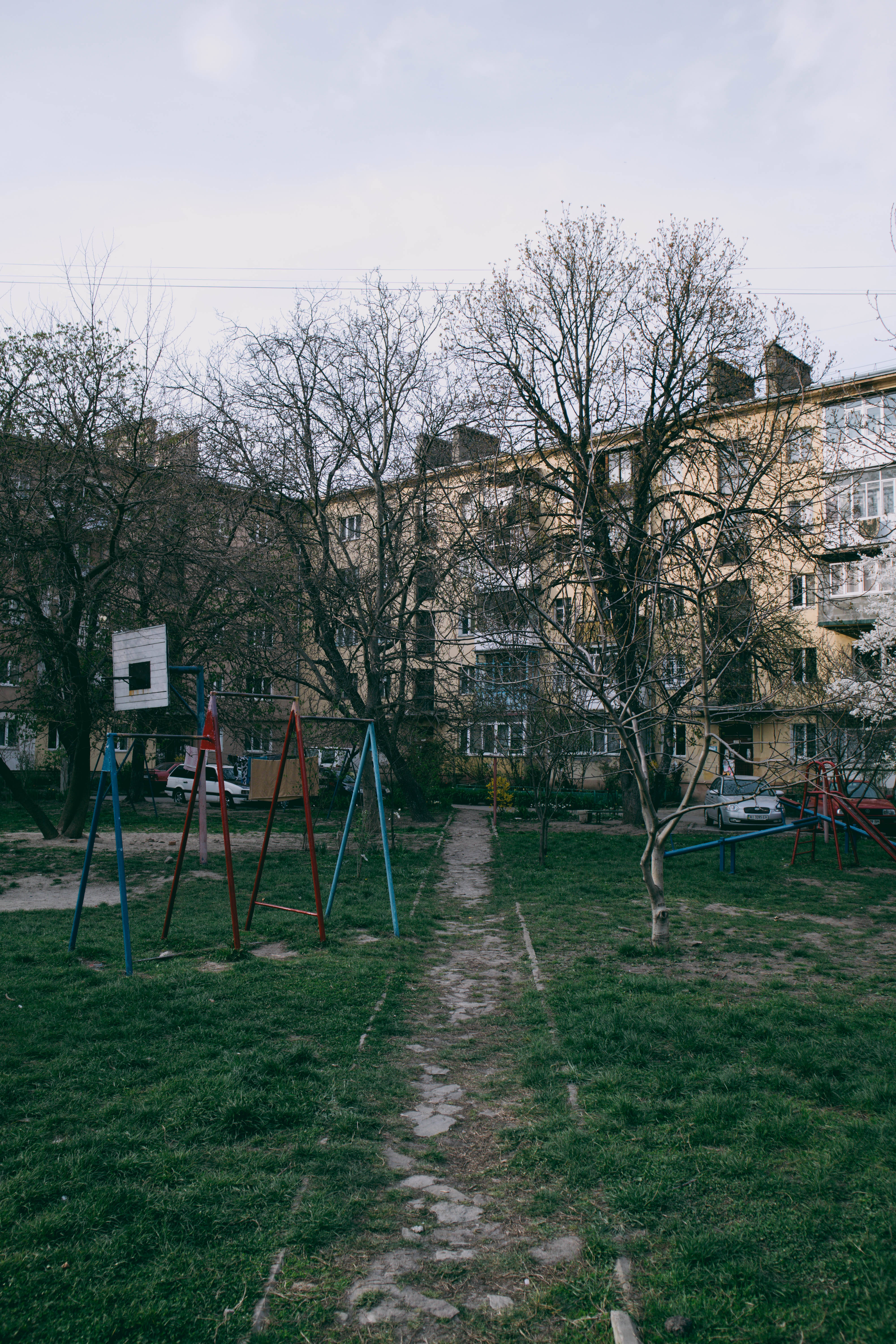 Playground 桌布 壁紙 — 一個寧靜的城市遊樂場，有色彩繽紛的遊樂設施和光禿禿的樹木，前面是一棟風化的公寓大樓，天空多雲。