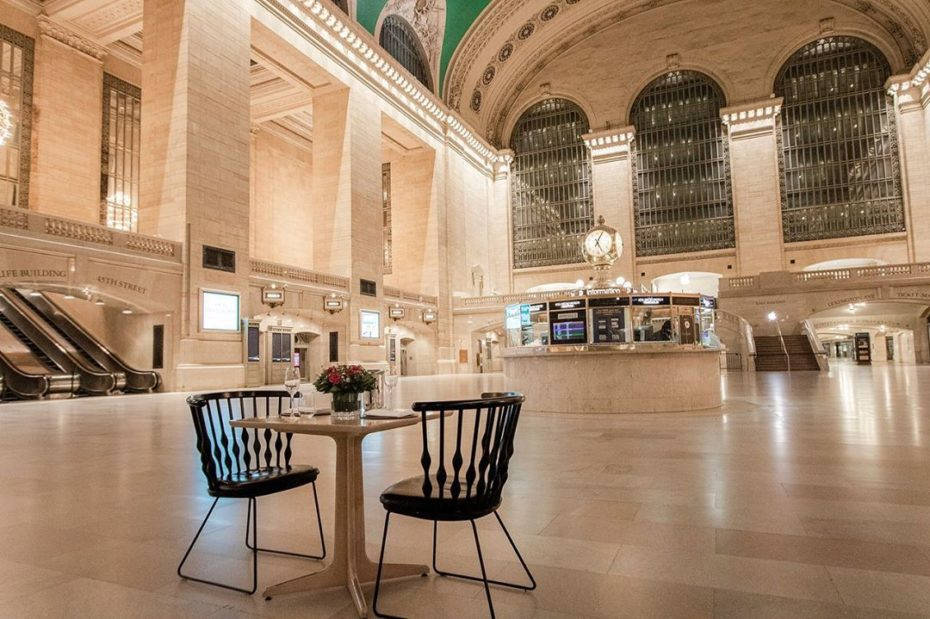 New York 桌布 壁紙 — 一個寧靜的大型火車站大廳，高拱窗和華麗天花板下有一張木桌和黑色椅子。