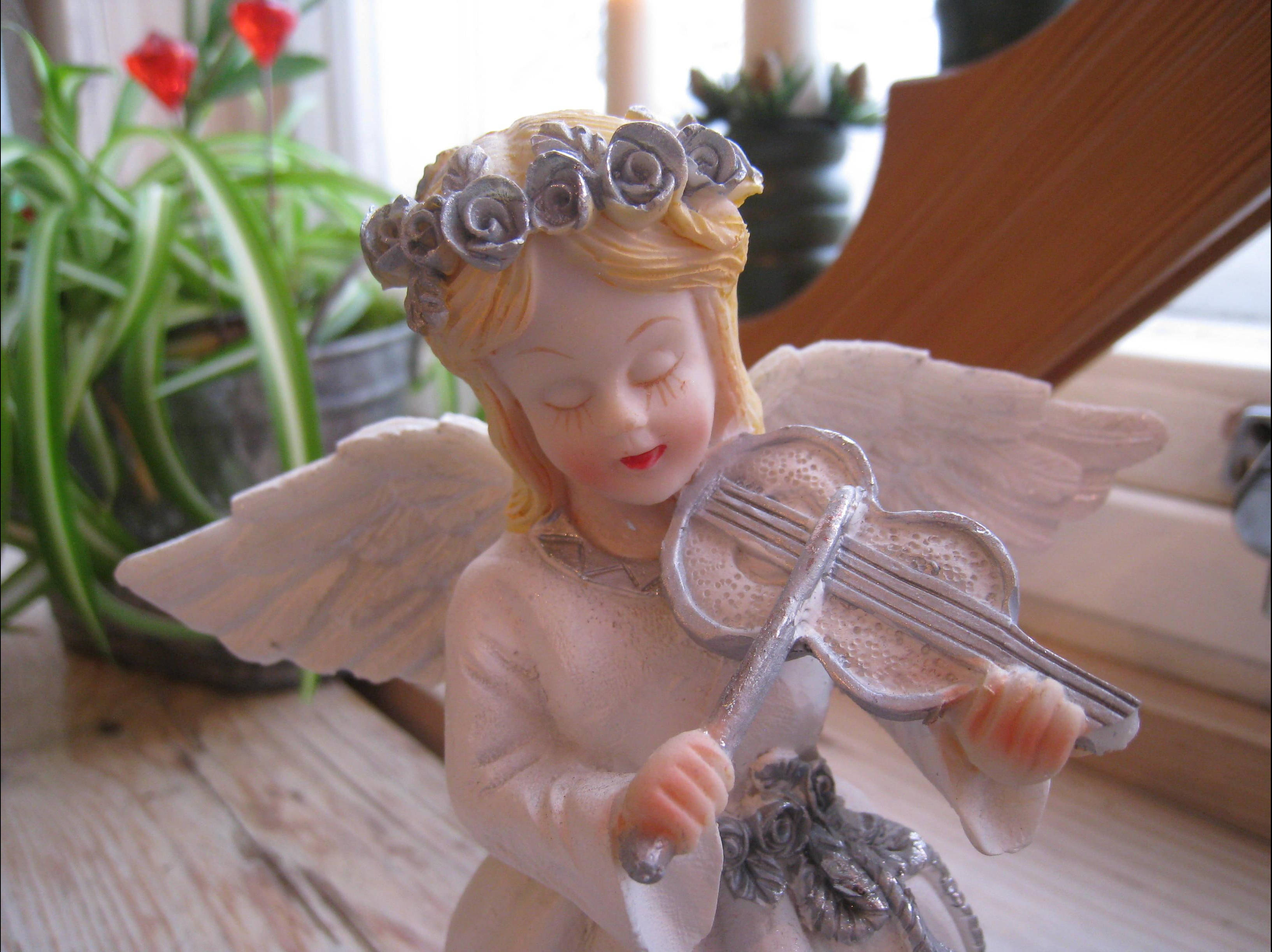 angels 桌布 壁紙 — 一個寧靜的天使雕像，戴著玫瑰冠冕和翅膀，在木製窗台上拉小提琴，旁邊有綠色植物。