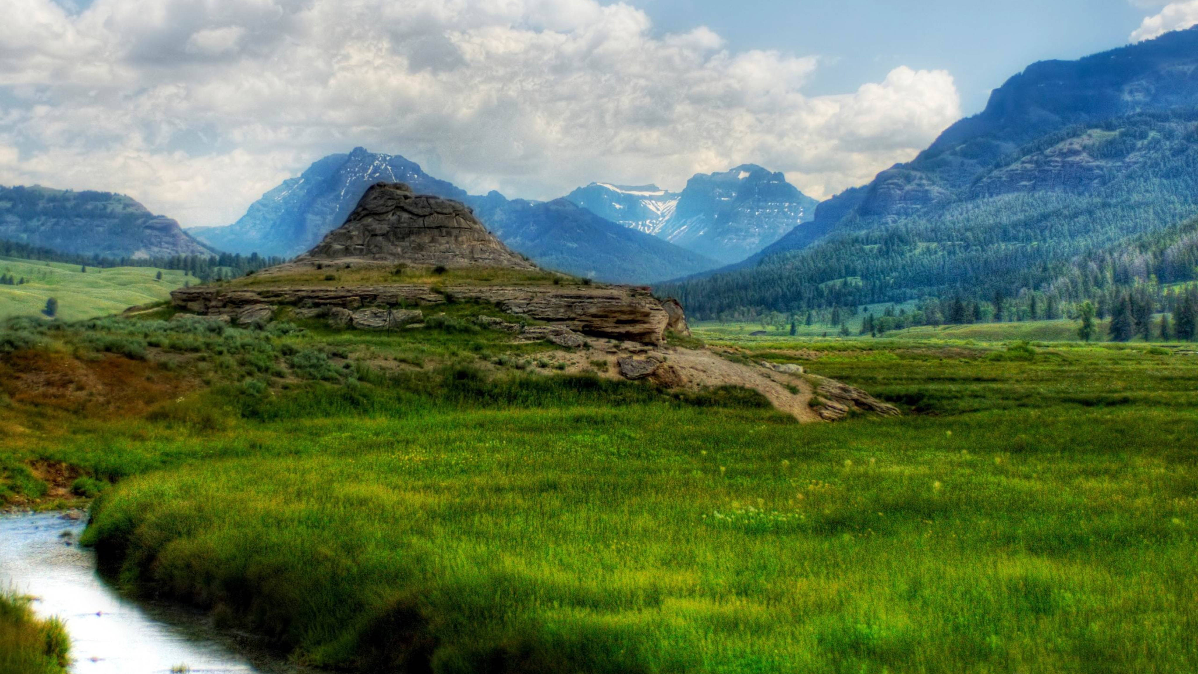 Yellowstone 桌布 壁紙 — 一個寧靜的山谷，蜿蜒的小溪流過岩石露頭，天空部分多雲。